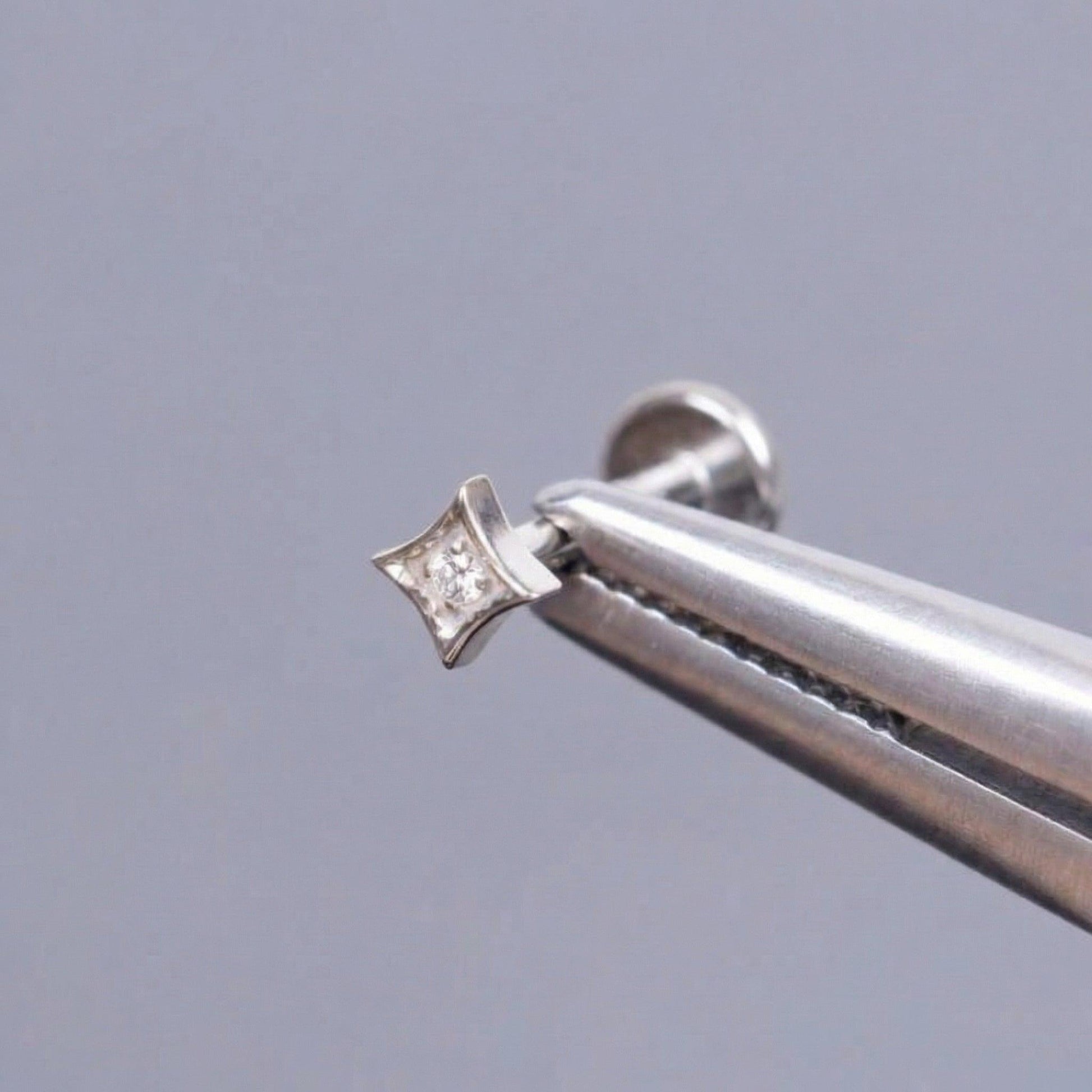 Silver medical-grade titanium piercing held securely by metal tweezers.