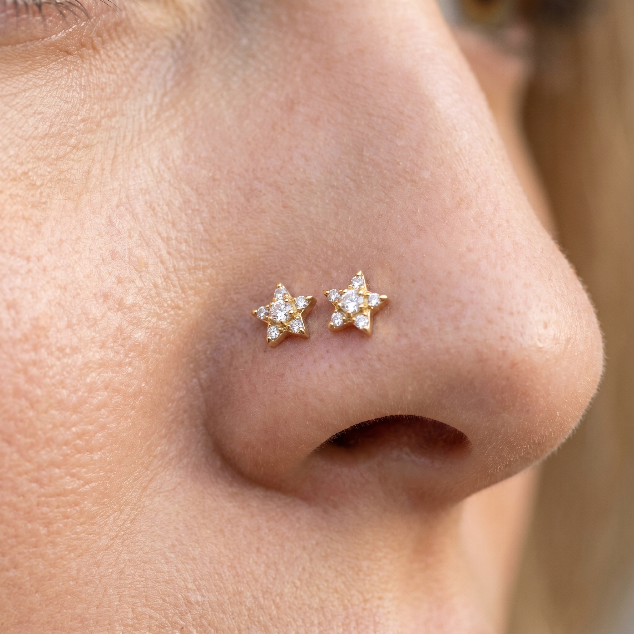Two gold star nose studs styled as a double nose piercing on one nostril