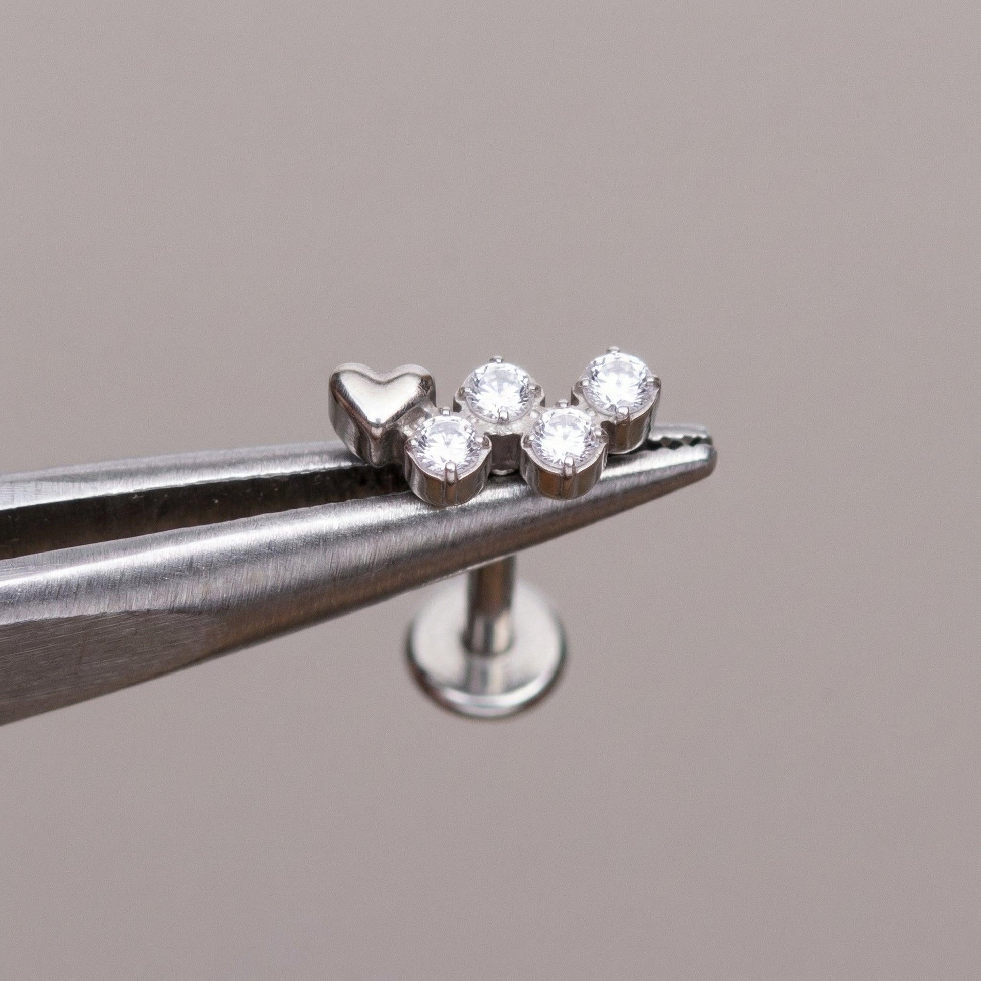 Silver heart cz cluster stud held securely by professional piercing tweezers.