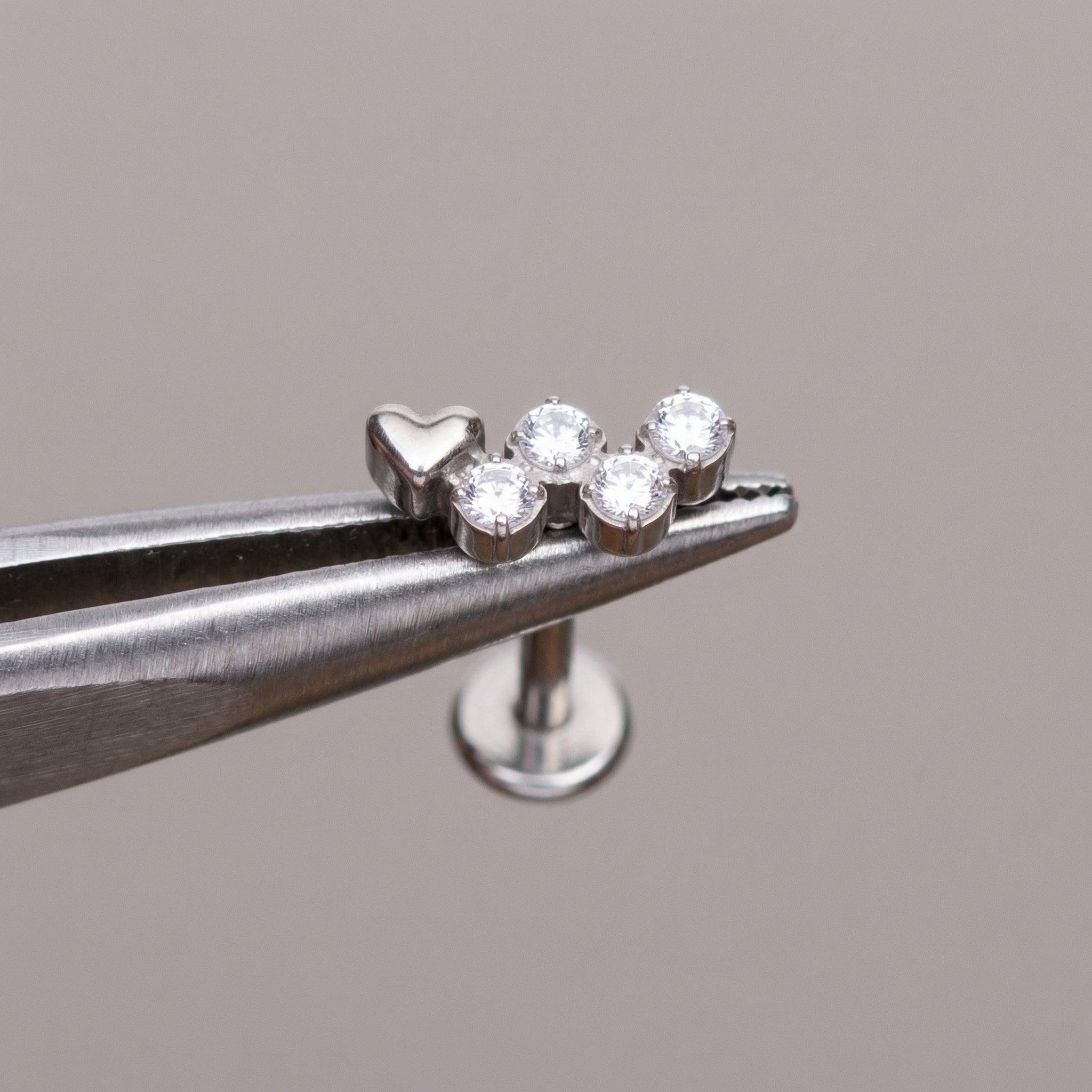 Silver heart cz cluster stud held securely by professional piercing tweezers.