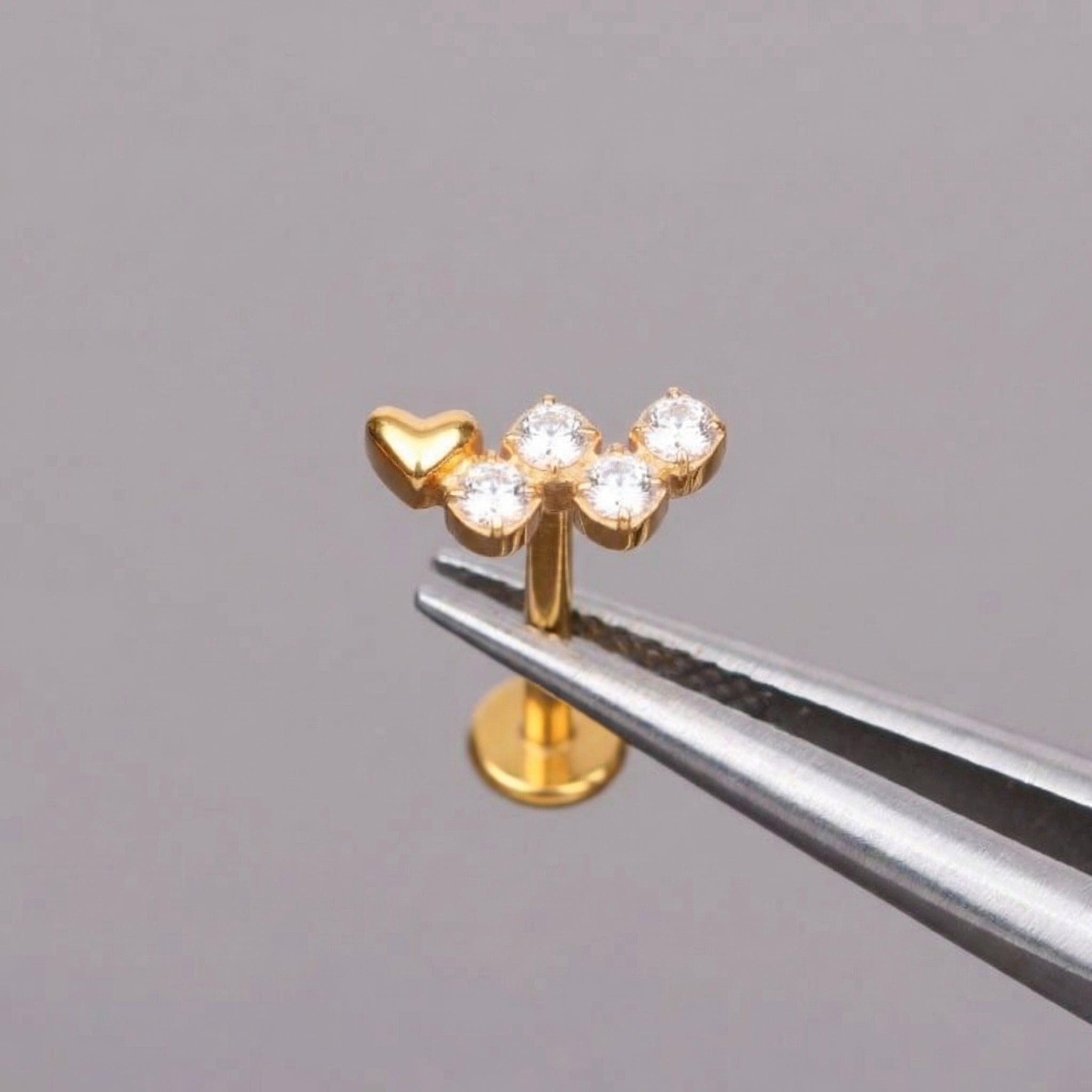 Gold heart clear stone cluster stud held safely with metal piercing tweezers.