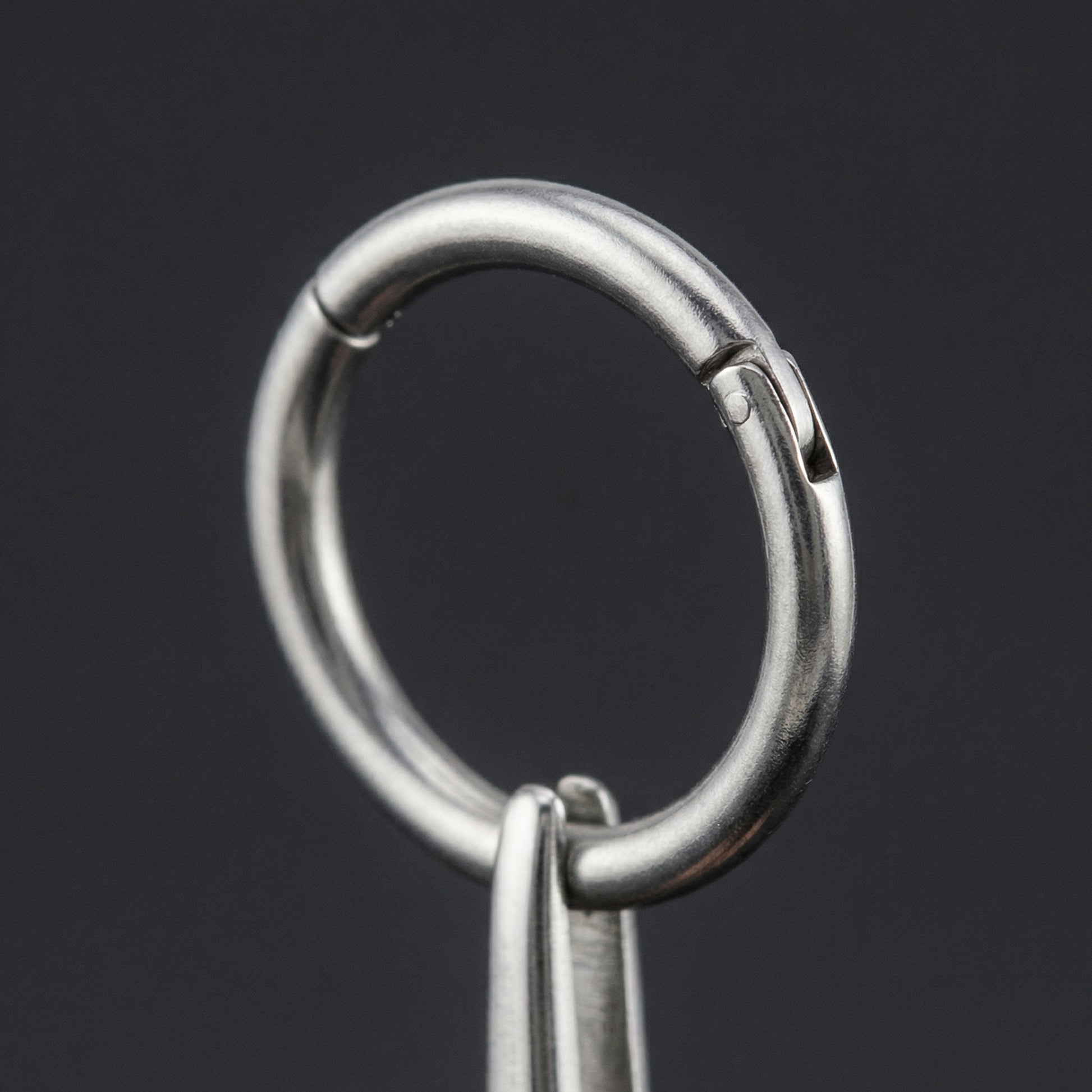 Surgical steel pliers holding a secure silver titanium hinged clicker ring close