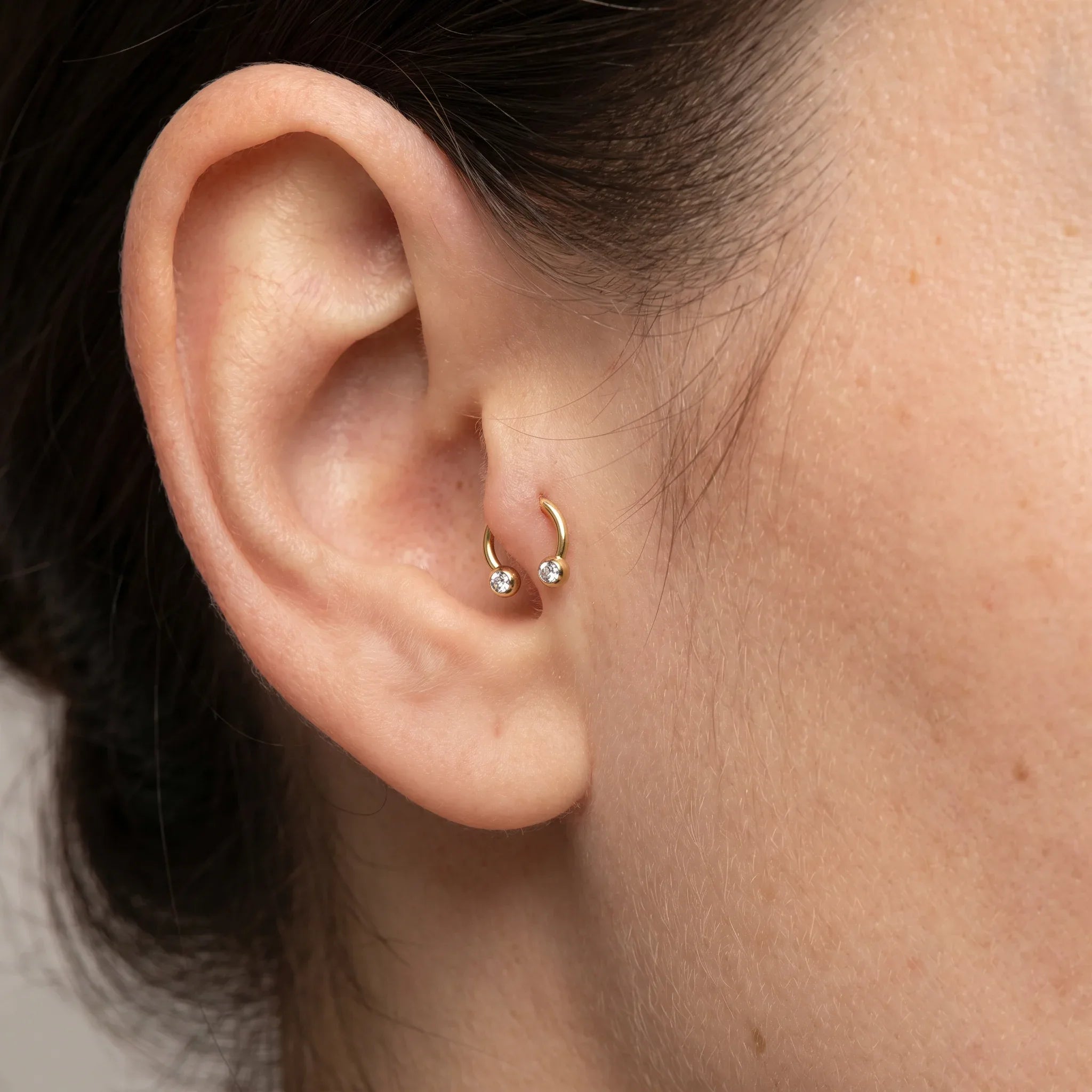 Gold titanium crystal ball horseshoe ring worn in a female piercing.