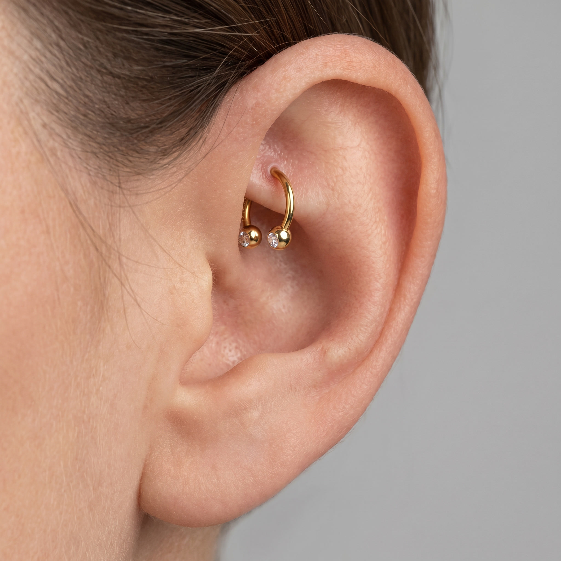 Gold titanium crystal ball horseshoe ring worn in a female rook ear piercing.