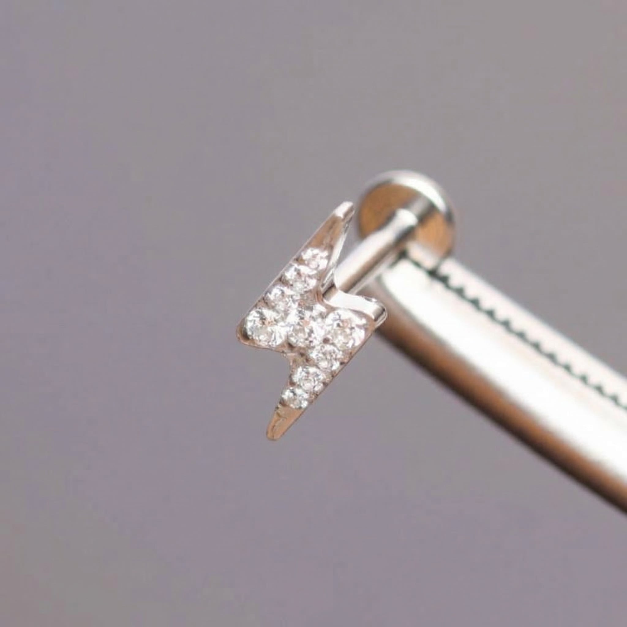 Silver lightning bolt held by professional piercing tool.
