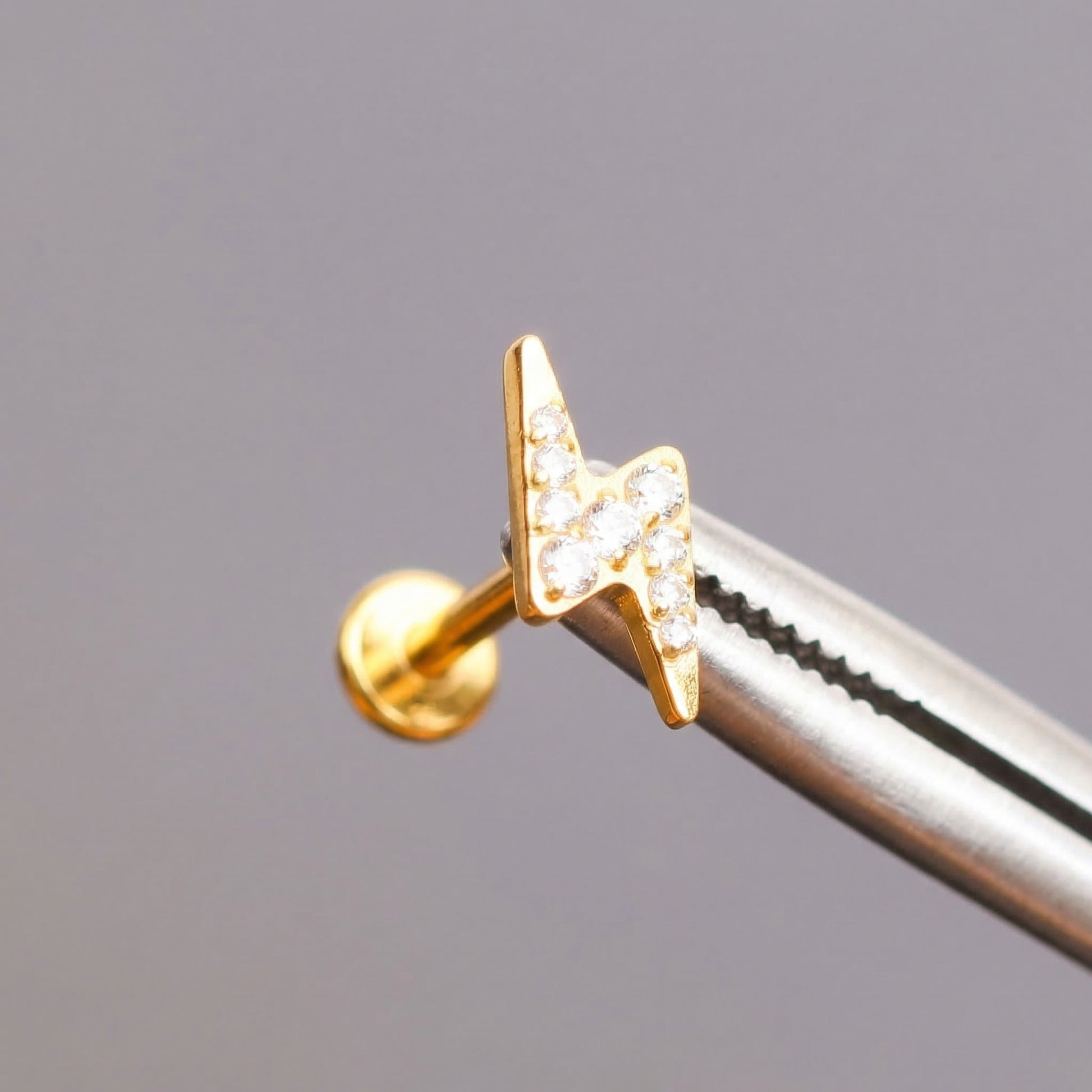 Gold lightning bolt held by professional piercing tool.