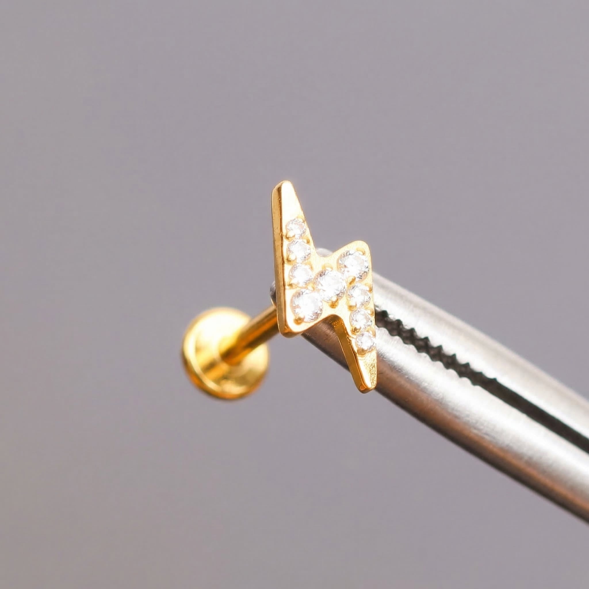Gold lightning bolt held by professional piercing tool.