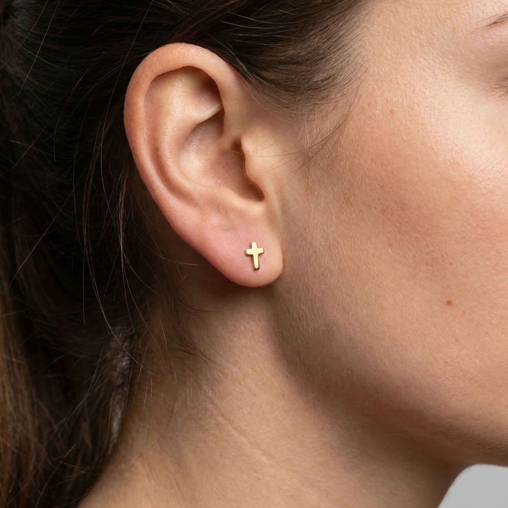 Gold minimal cross stud styled beautifully in a standard lower piercing.