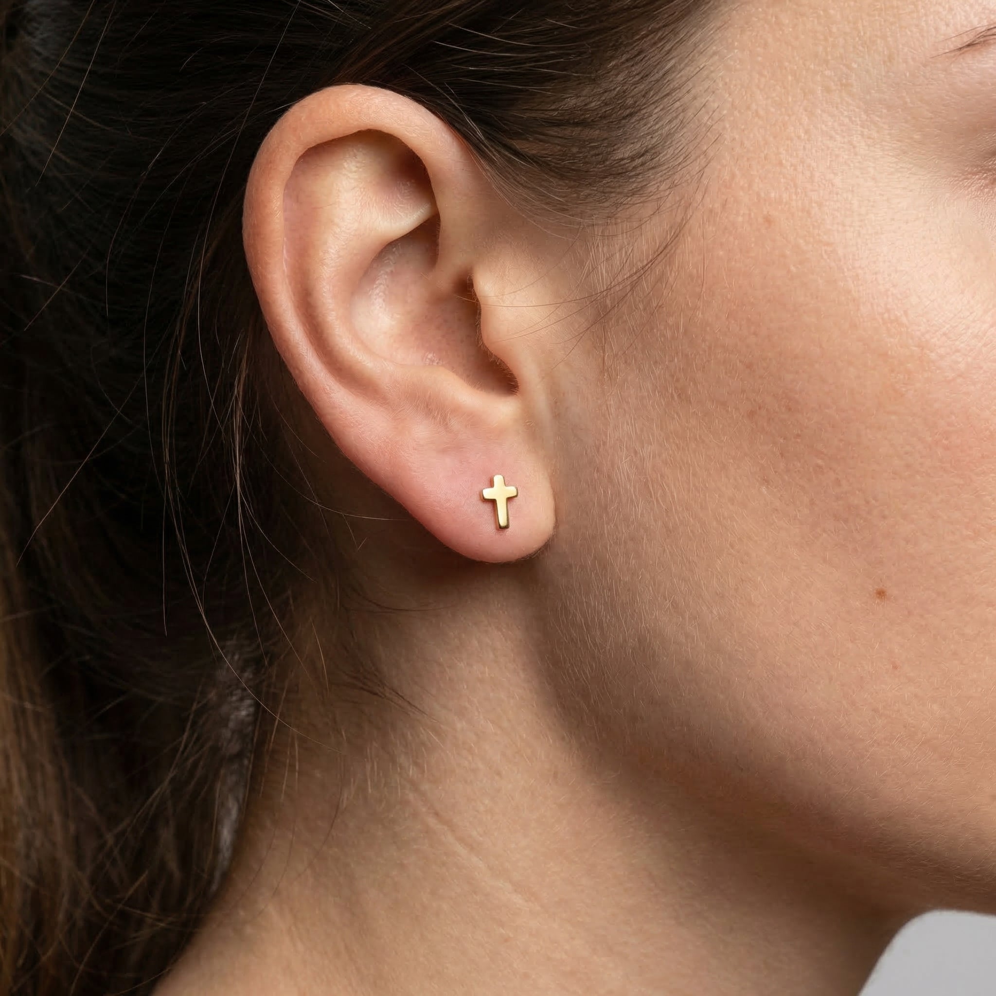 Gold minimal cross stud styled beautifully in a standard lower piercing.