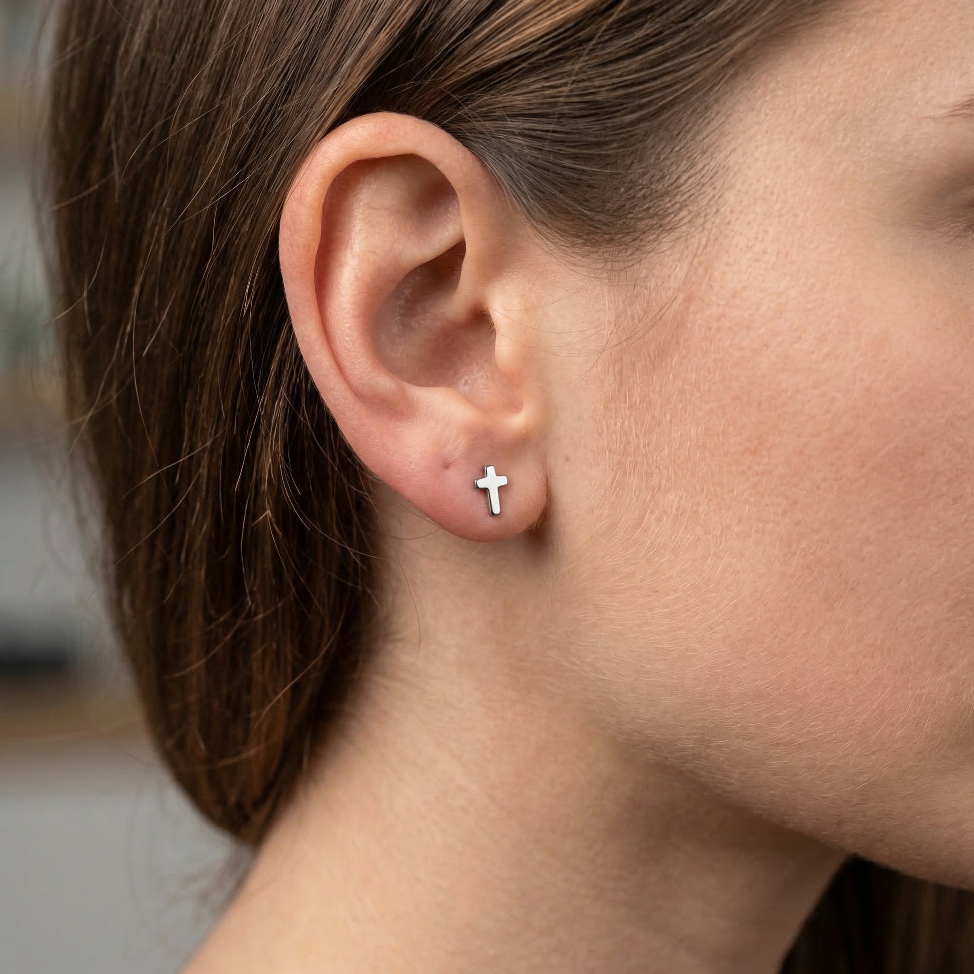 Silver minimal cross cartilage earring worn gracefully in a standard lower placement.