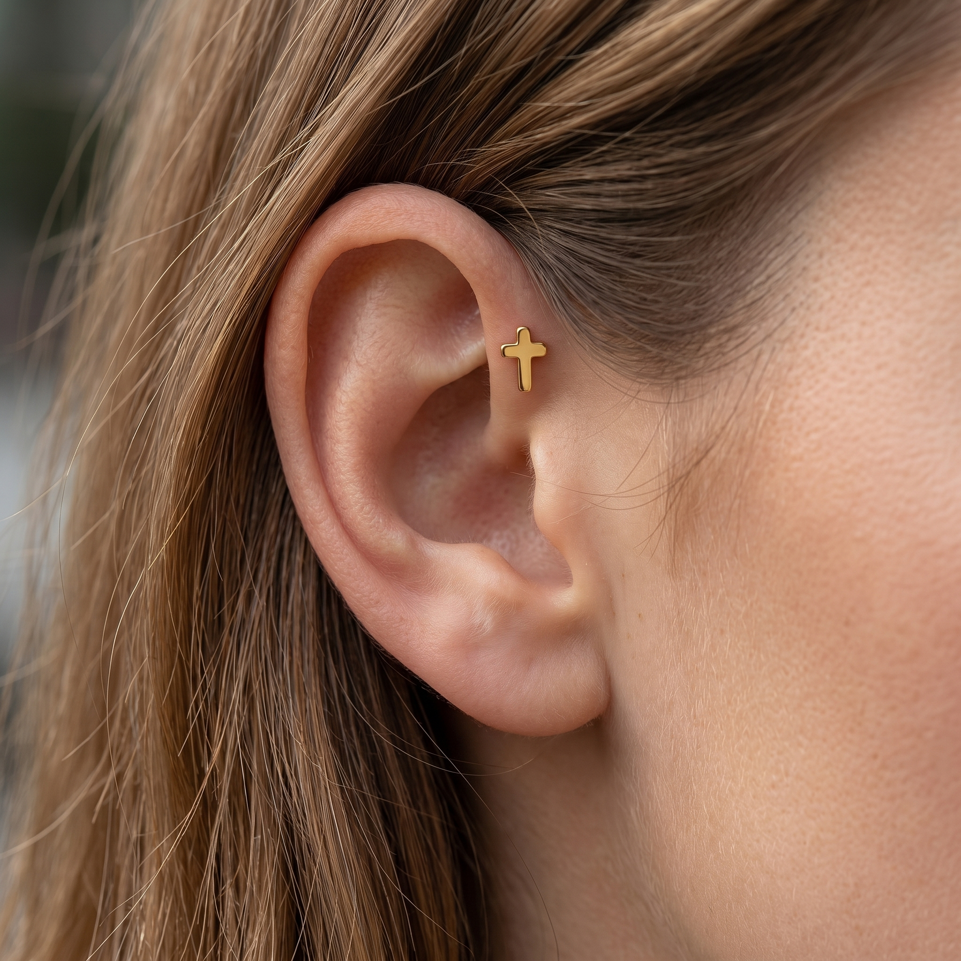 Gold minimalist cross cartilage earring worn securely in a piercing.