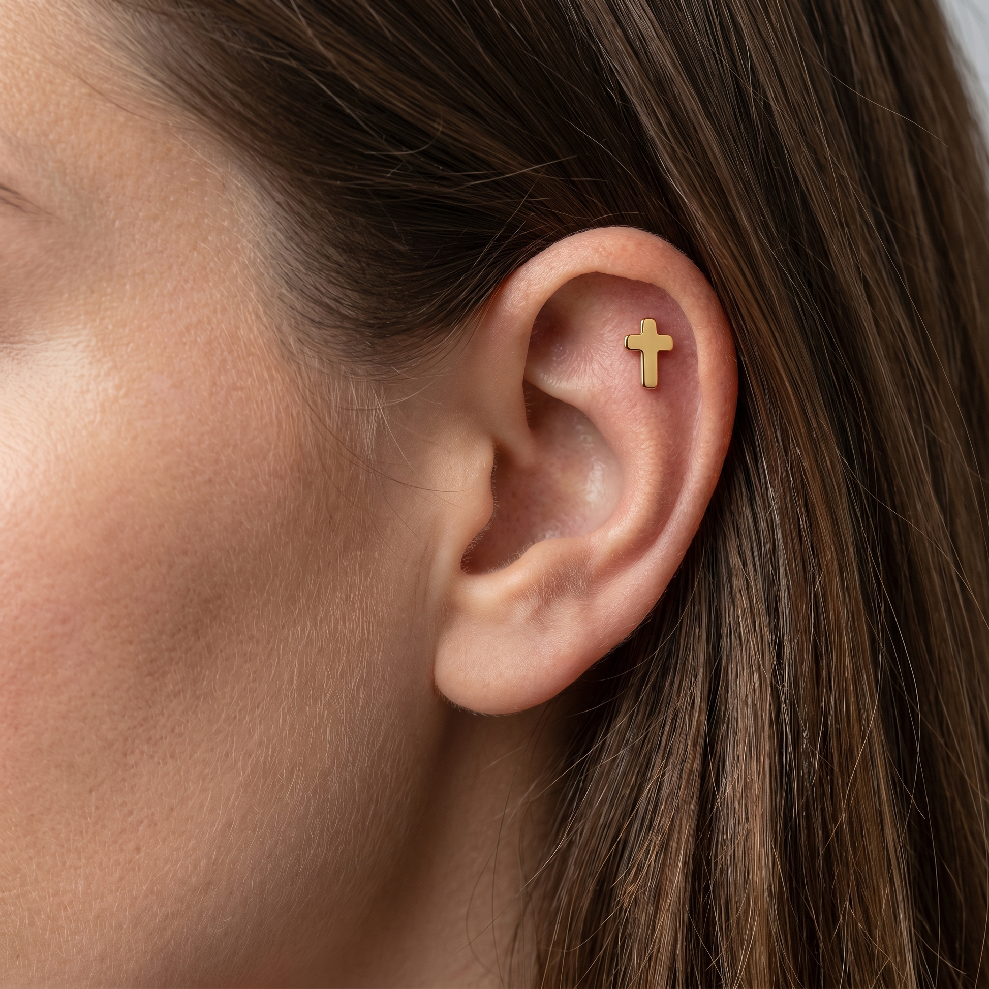 Gold cross stud styled elegantly in an upper cartilage piercing.
