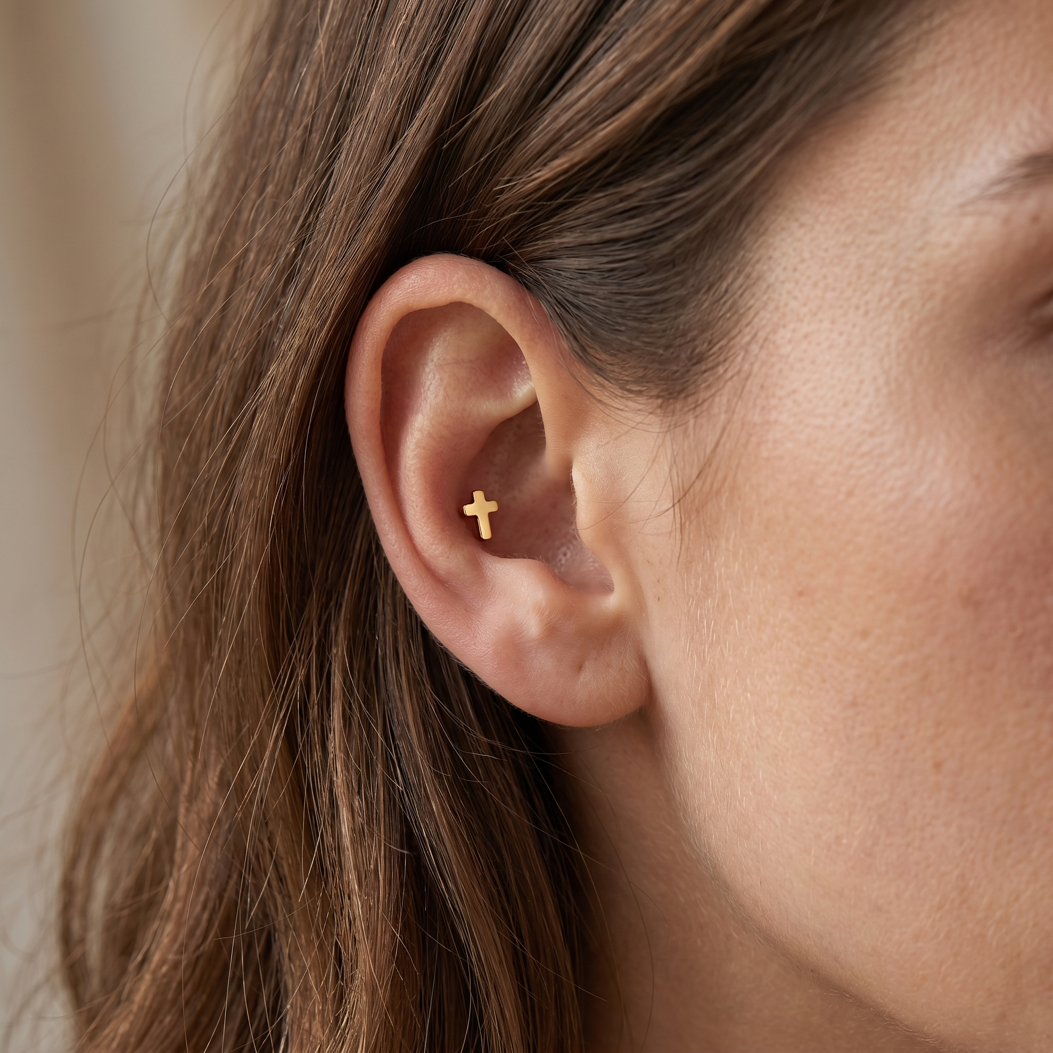 Gold cross ear piercing jewelry styled inside an cartilage piercing.