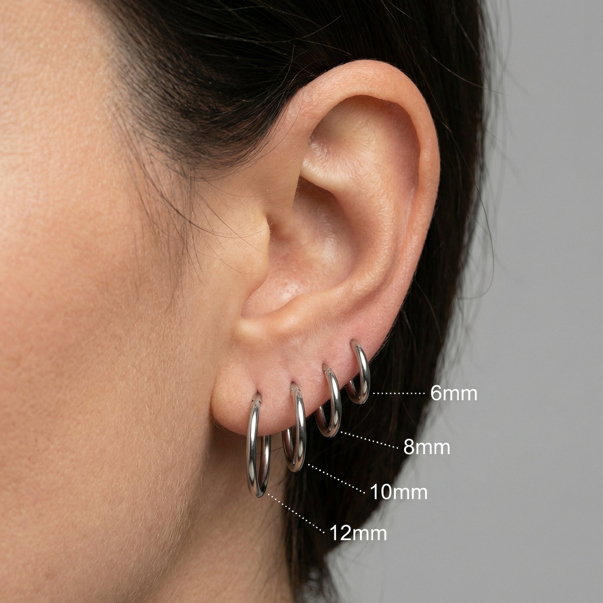 Stacked ear setup showing four silver titanium minimalist clicker hoops in sizes