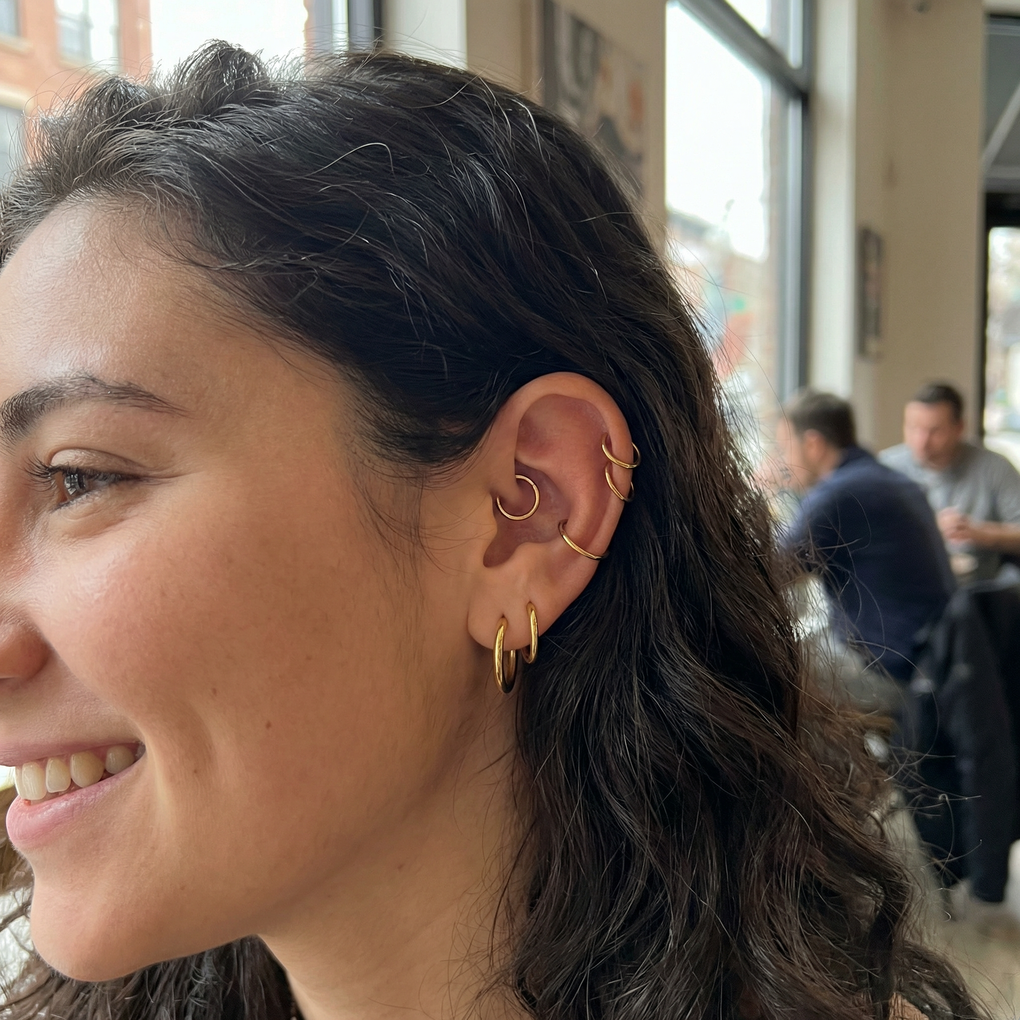 Smiling model showcasing a curated ear arrangement with a gold titanium clicker