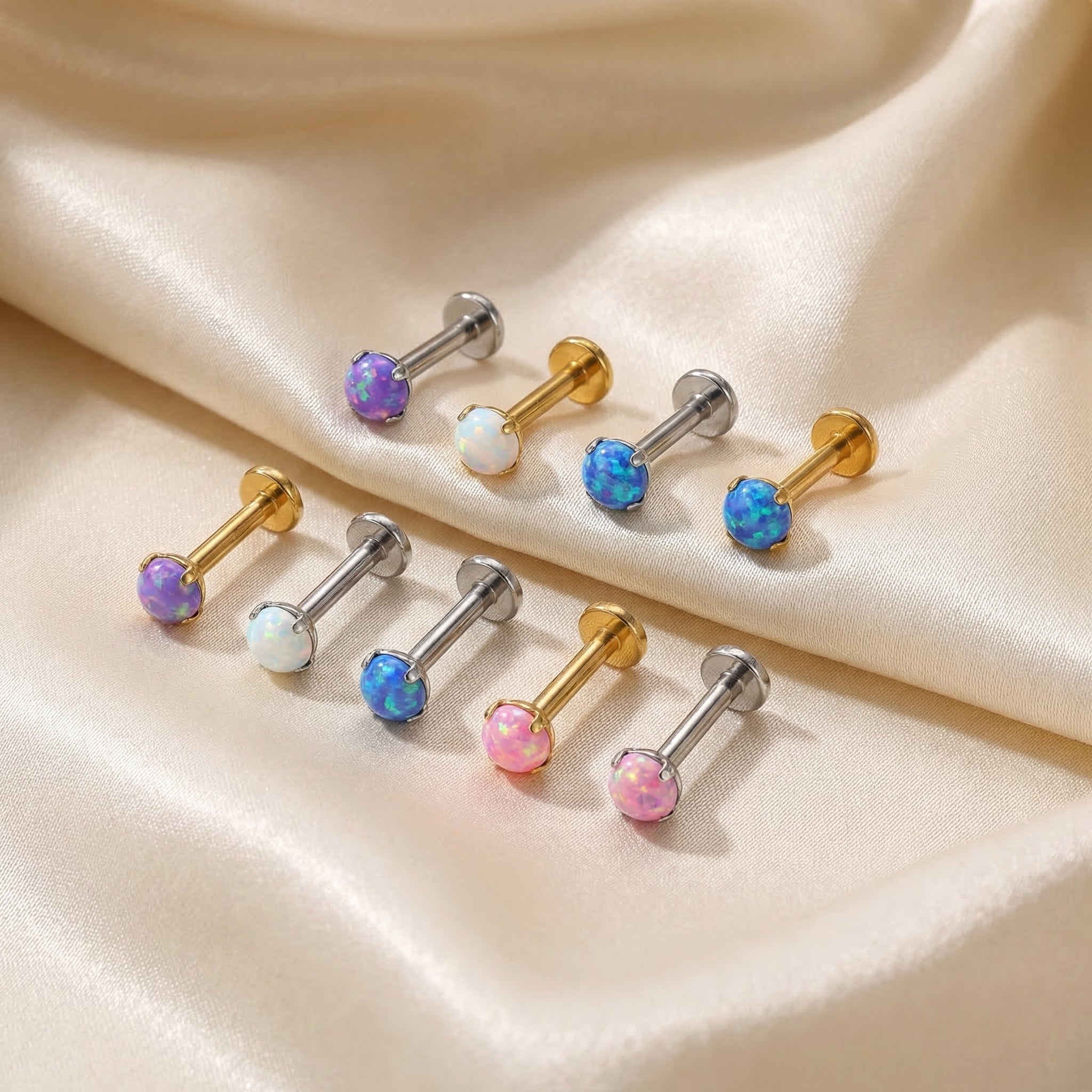 Various colors of opal piercing studs resting on white silk.