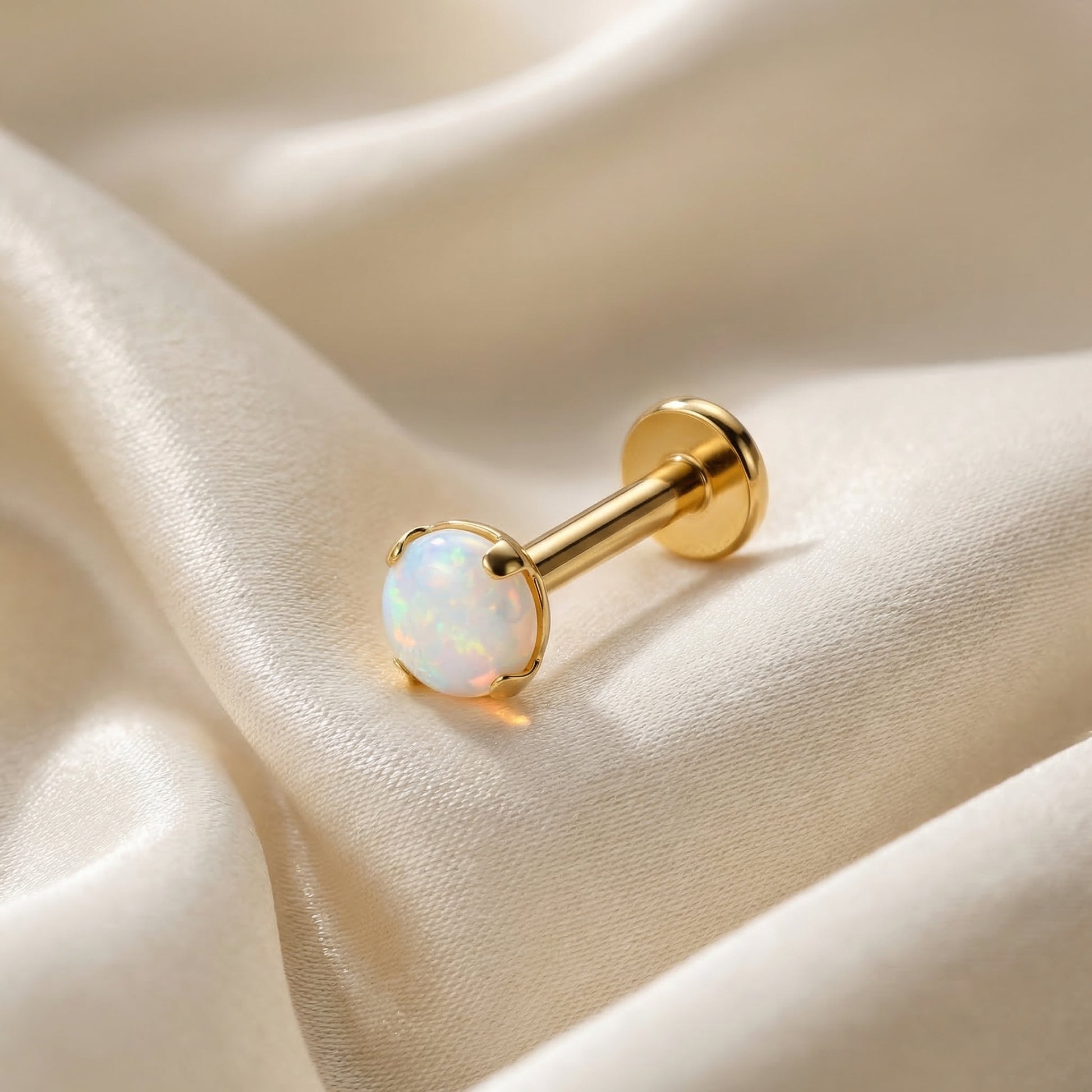 Gold medical-grade titanium white opal piercing on silk.