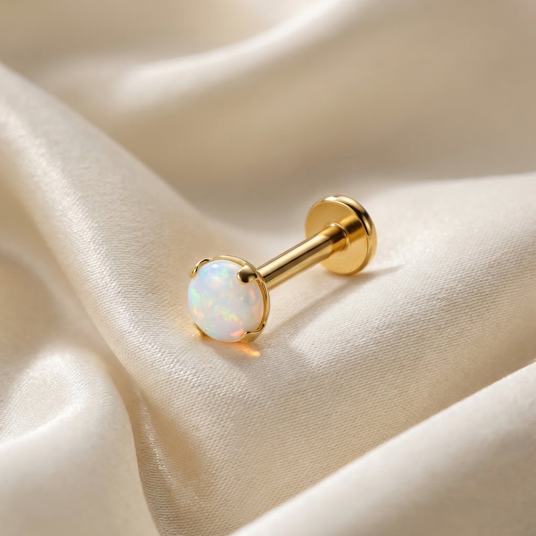 Gold medical-grade titanium white opal piercing on silk.