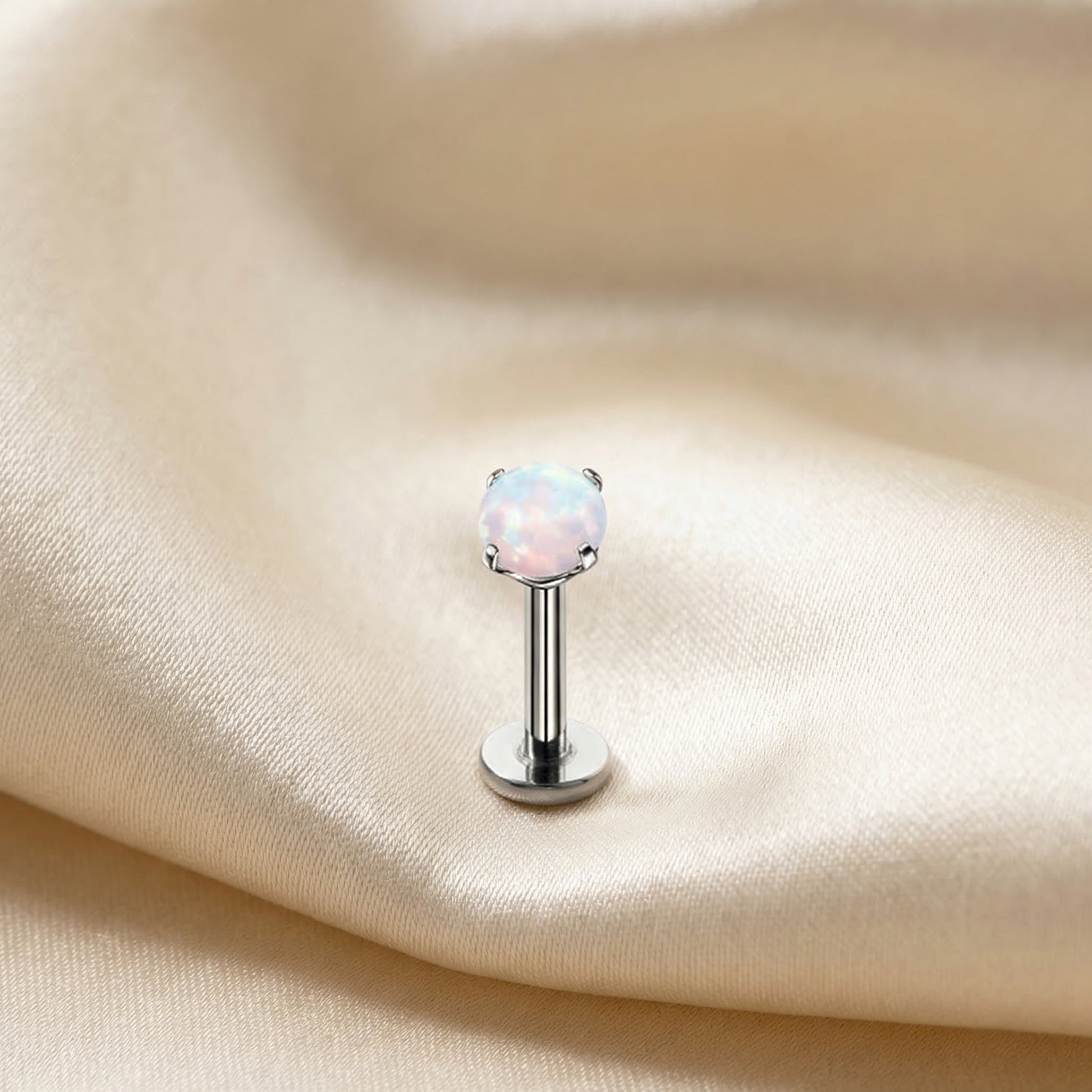 Silver medical-grade titanium white opal piercing on silk.