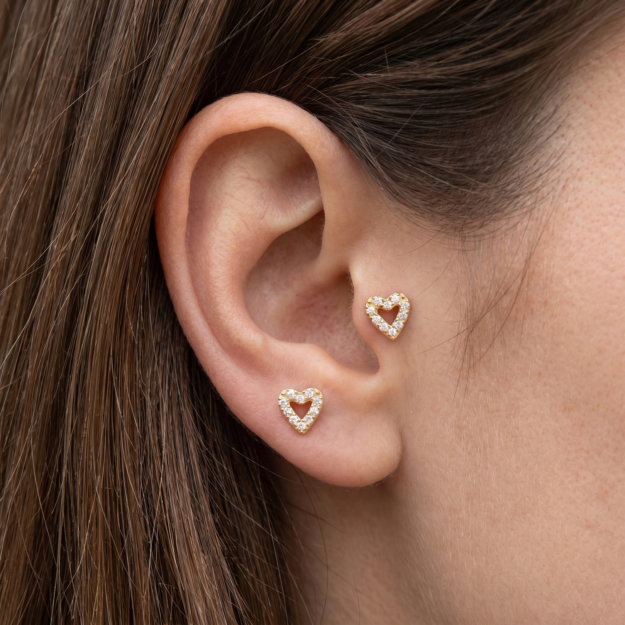 Gold paved heart and stud worn in an ear cartilage.