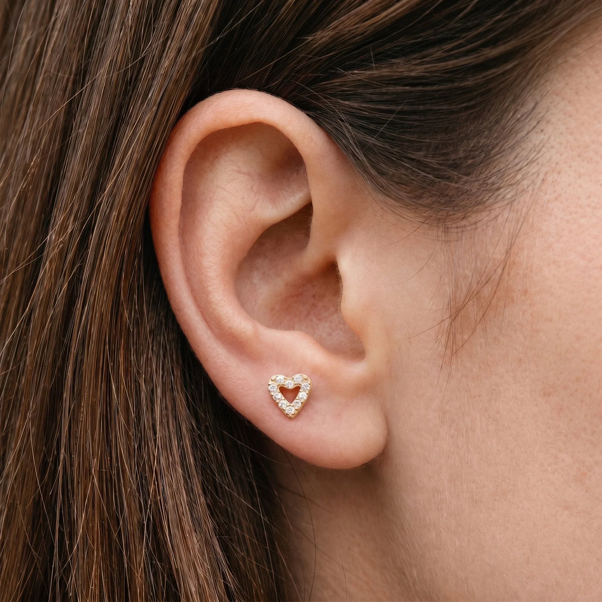 Gold paved heart stud worn in a female anti tragus piercing.