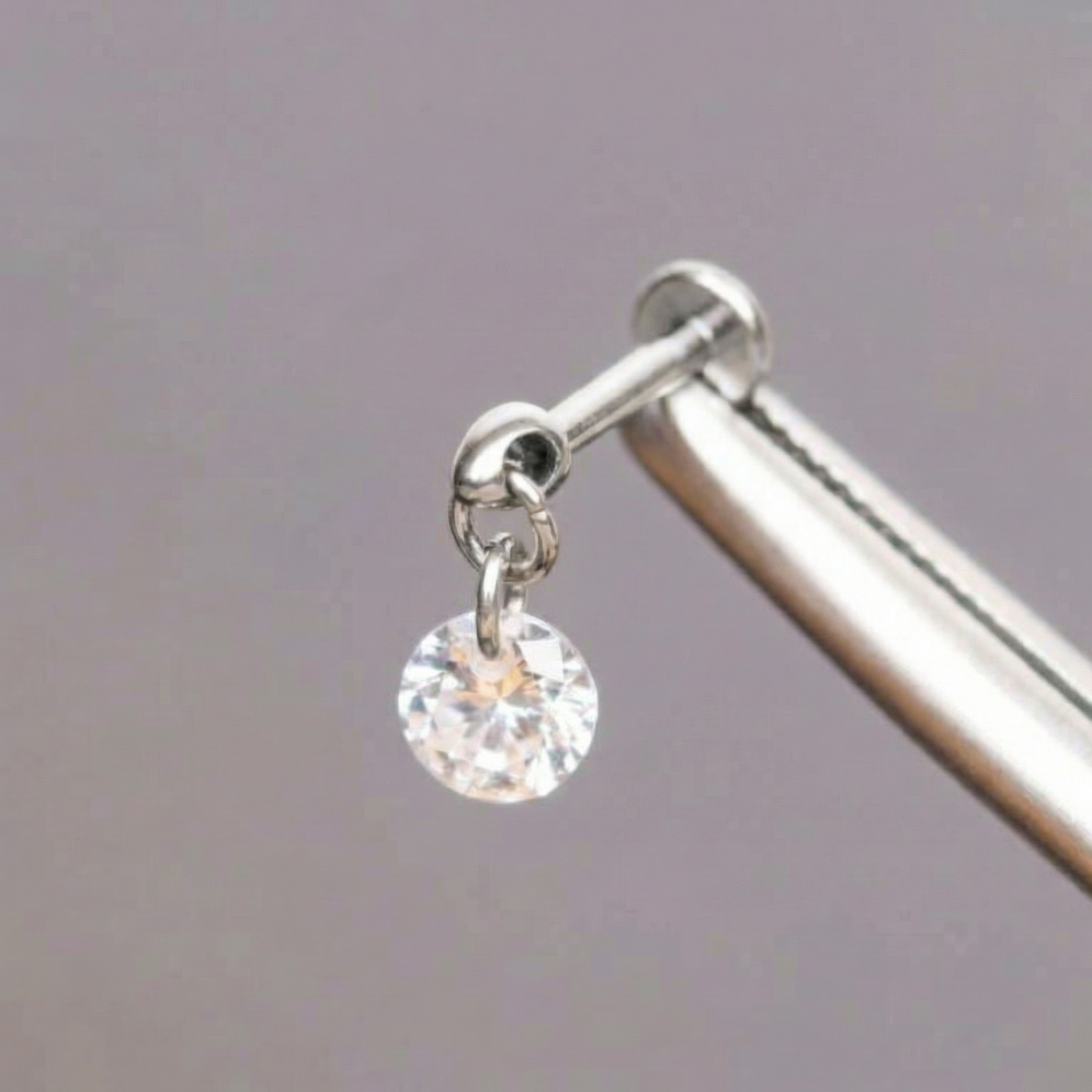 Surgical tweezers displaying a silver titanium round zircon dangle flat back labret.