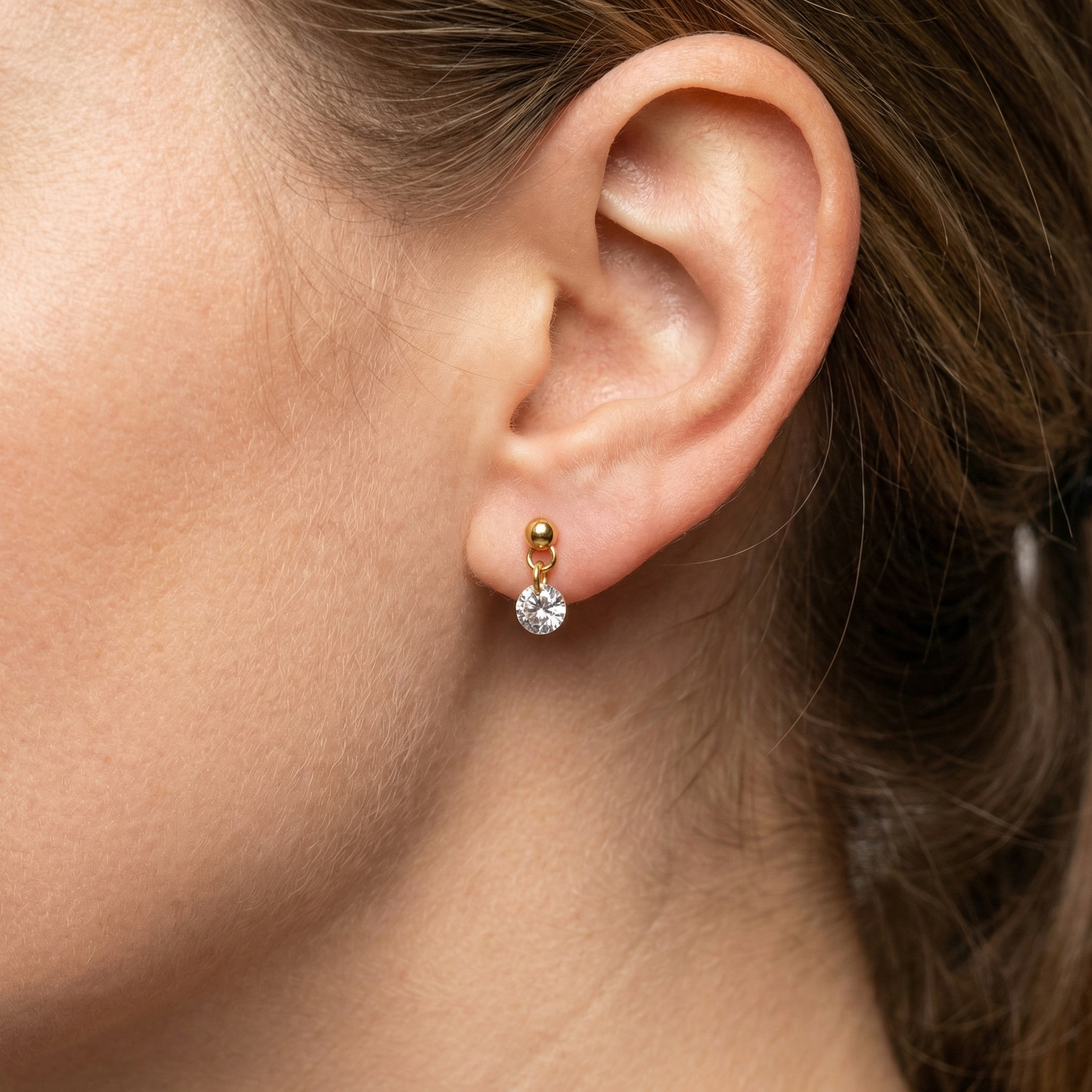 Model showcasing a gold round zircon dangle labret in her standard lower earlobe piercing.