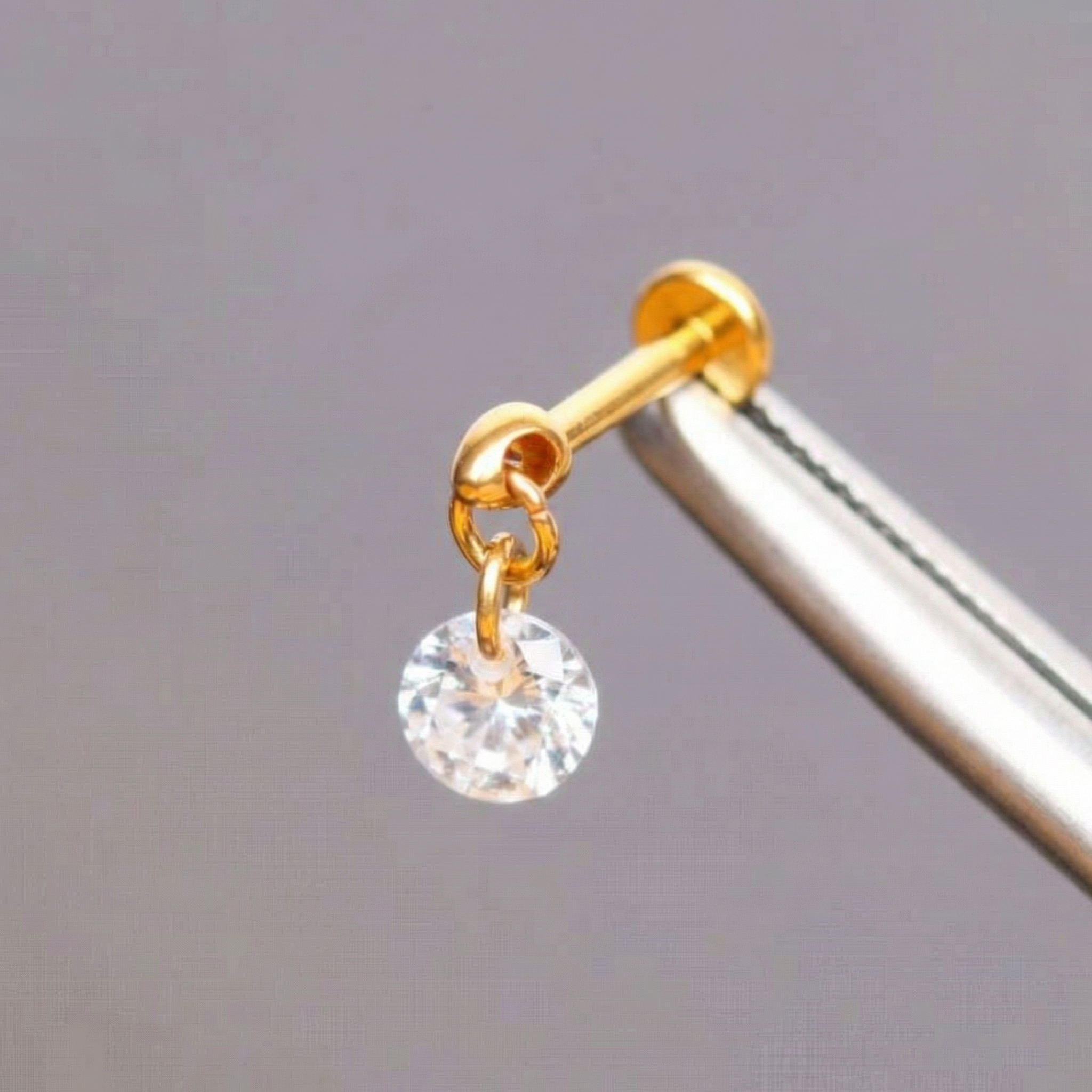 Precision tweezers holding a gold titanium round zircon dangle flat back labret.