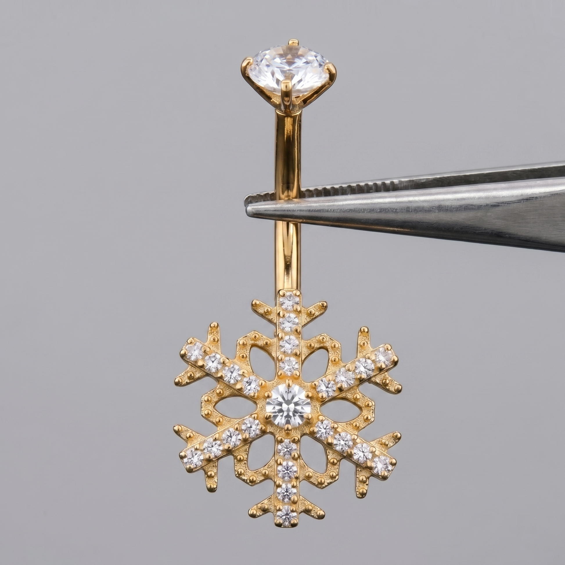 Gold snowflake cz belly button ring held by metal tweezers.