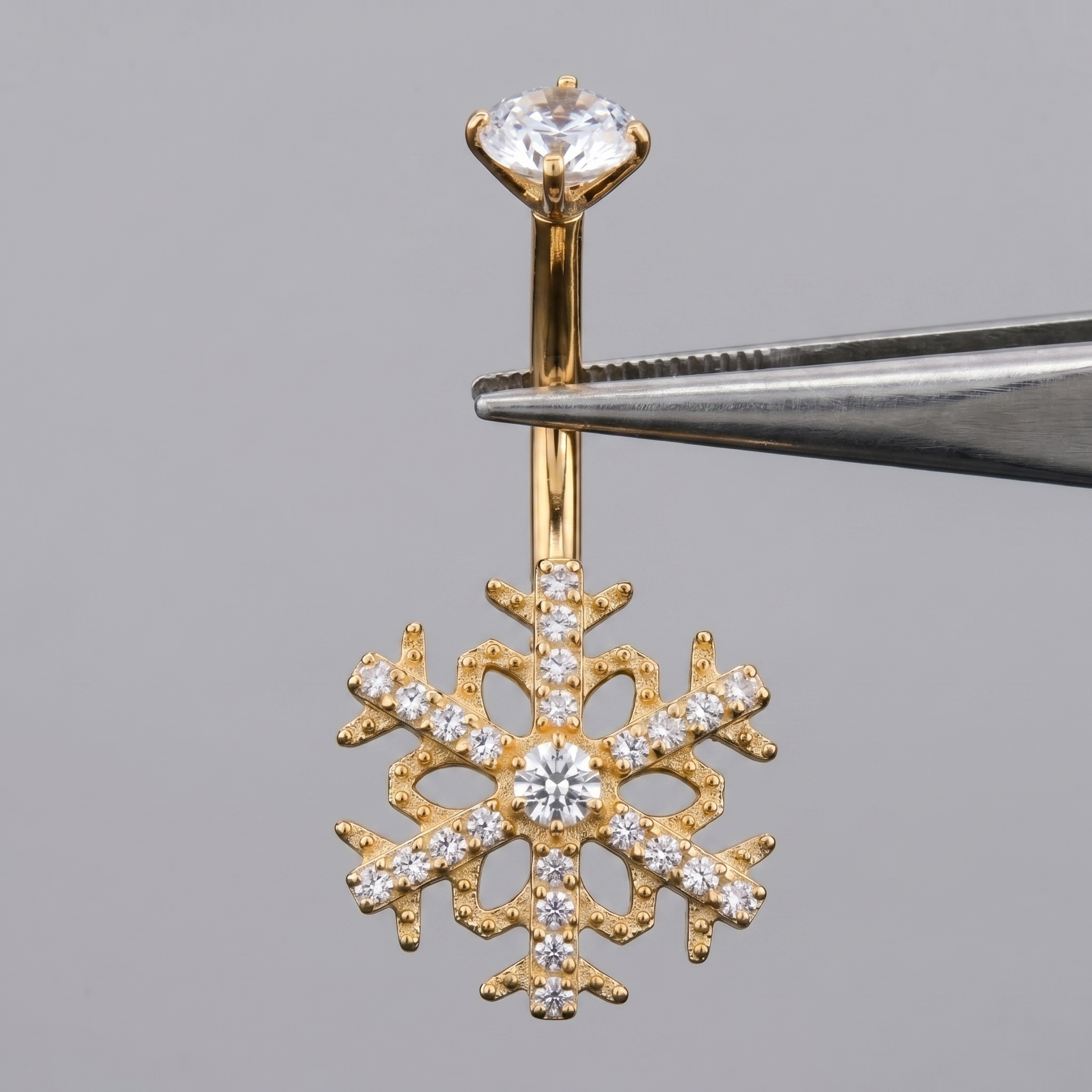 Gold snowflake cz belly button ring held by metal tweezers.