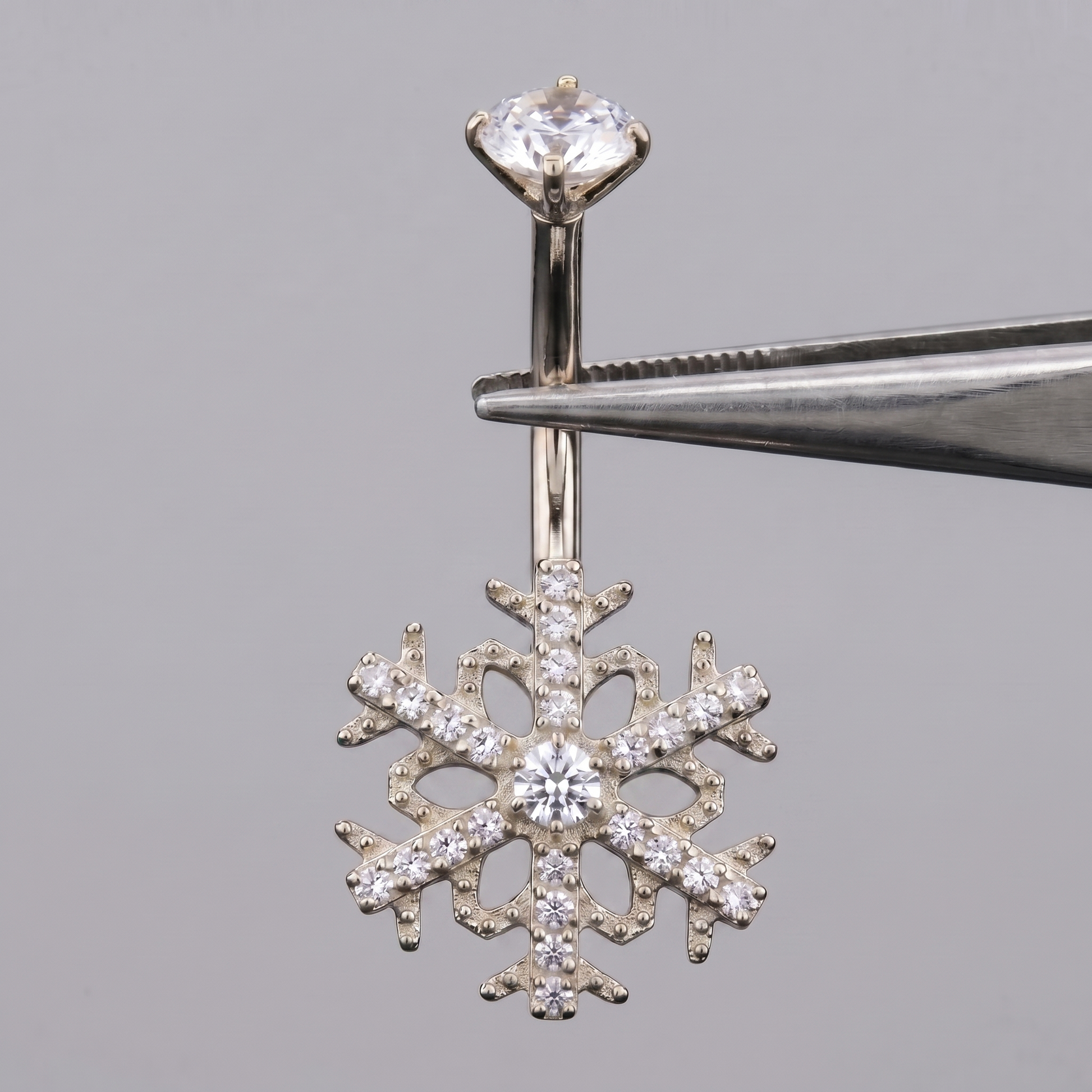Silver snowflake cz belly button ring held by metal tweezers.