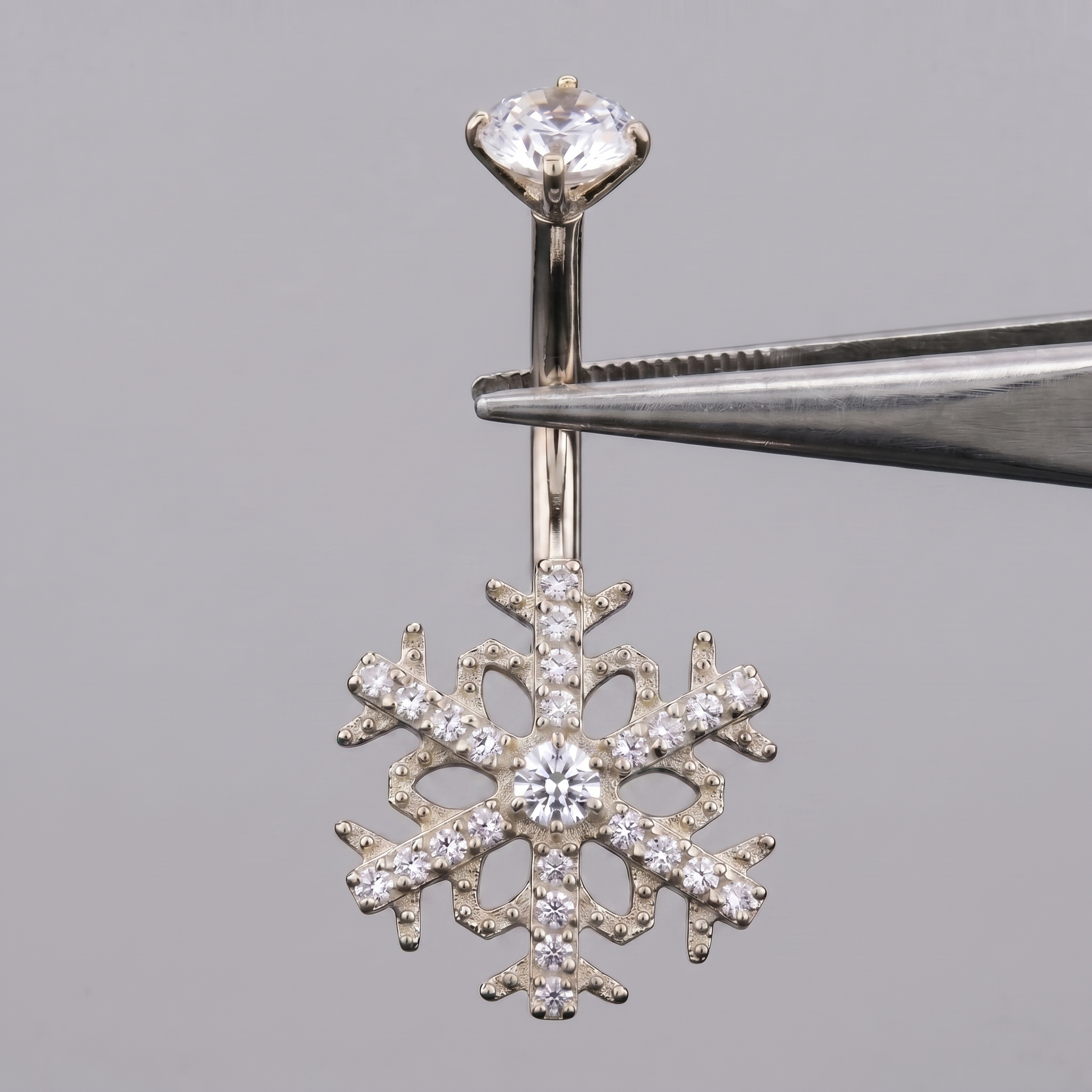 Silver snowflake cz belly button ring held by metal tweezers.