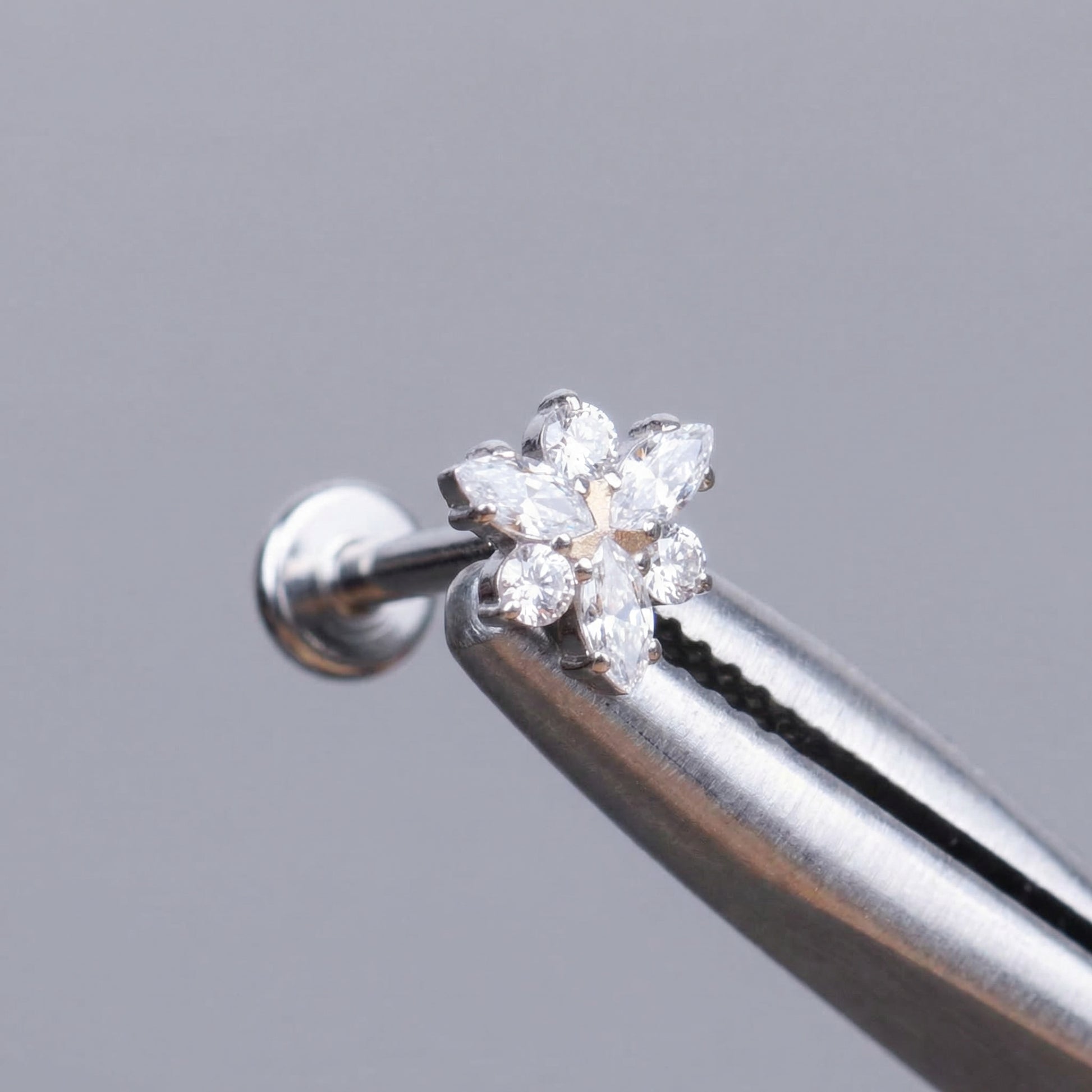 Silver elegant cartilage stud held securely by metal tweezers.