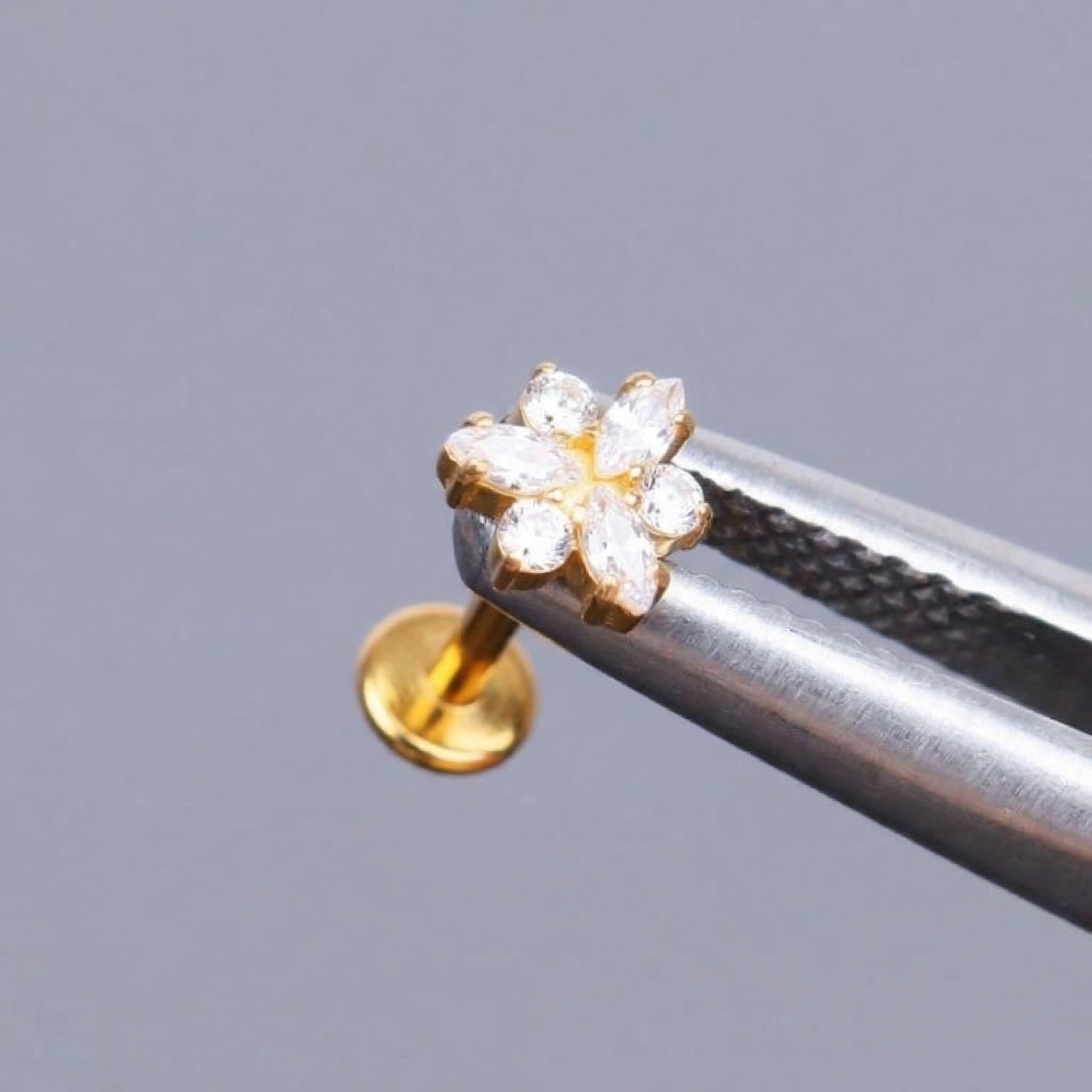 Gold snowflake zircon cluster held securely by metal tweezers.