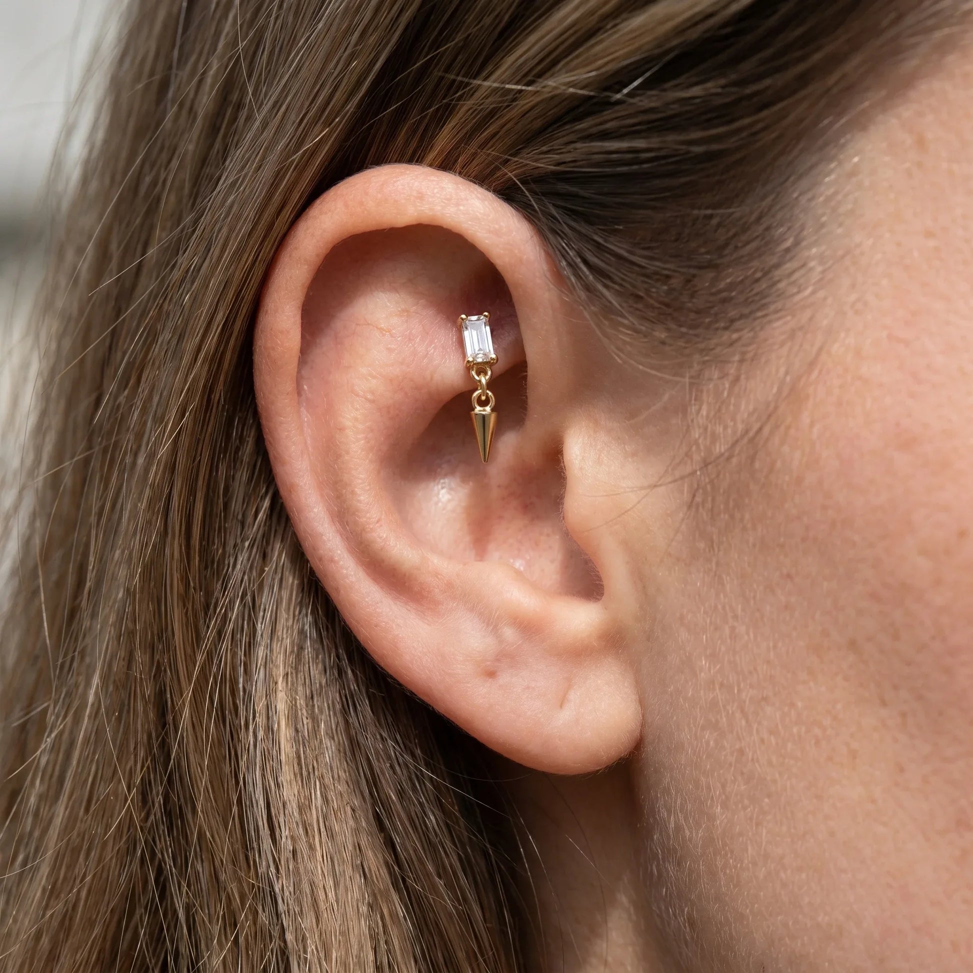 Gold spike dangle faux stud worn in a female ear.