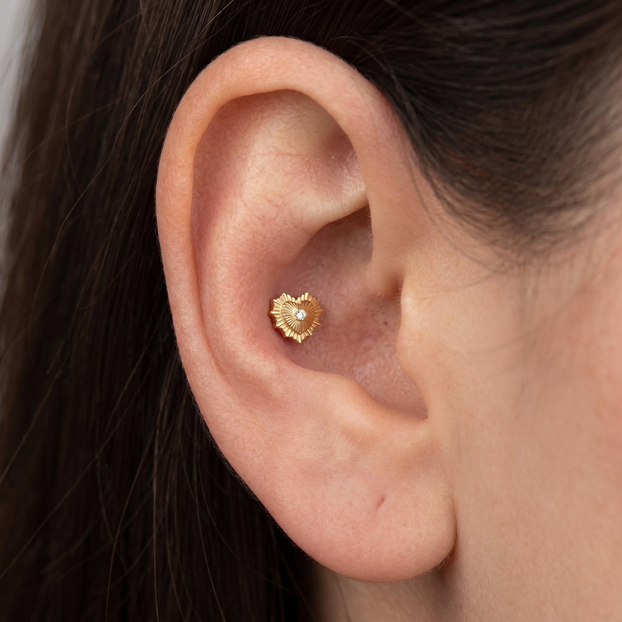 Gold sunburst heart resting elegantly inside a model's conch ear piercing.