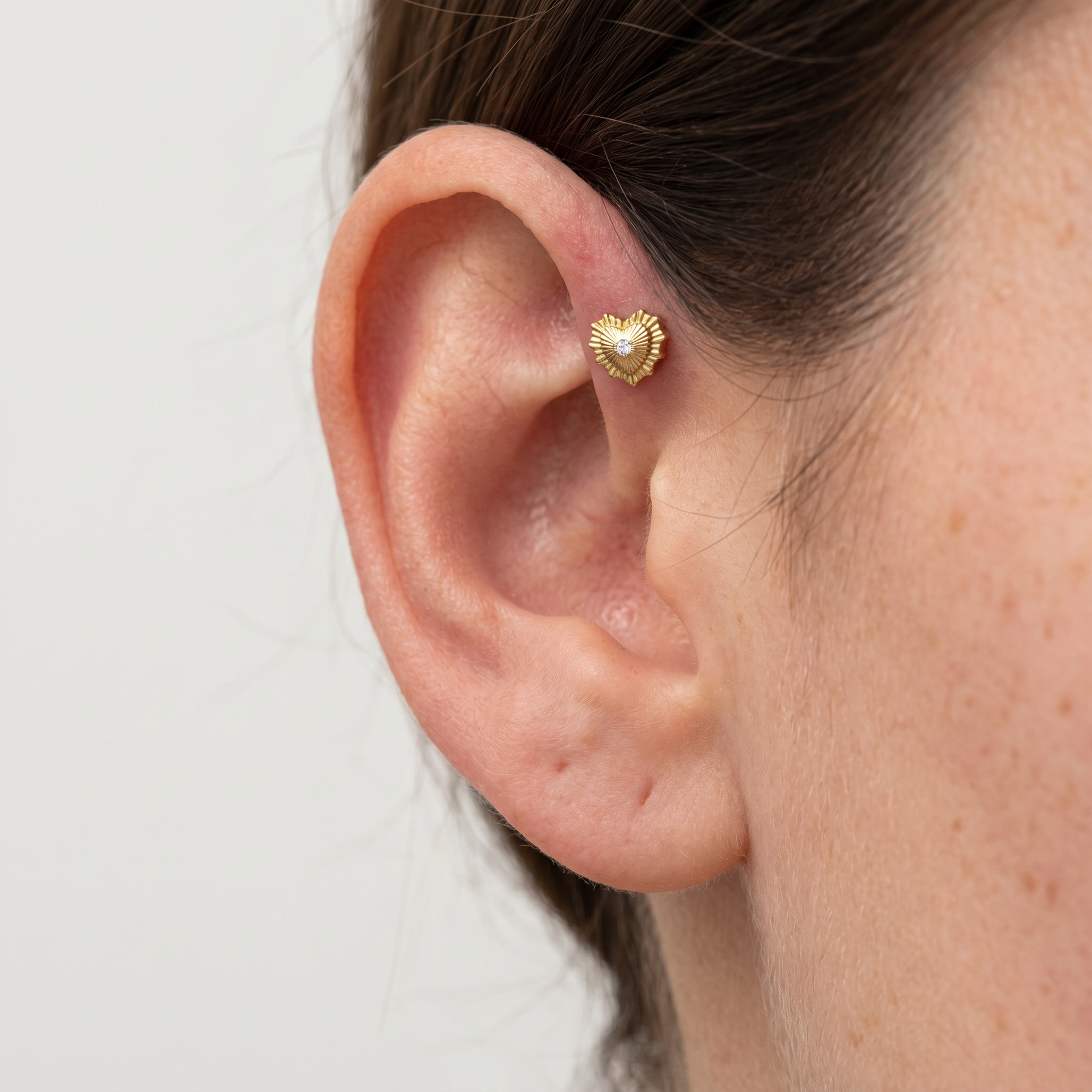 Gold sunburst heart cartilage stud styled cleanly in an upper cartilage placement.
