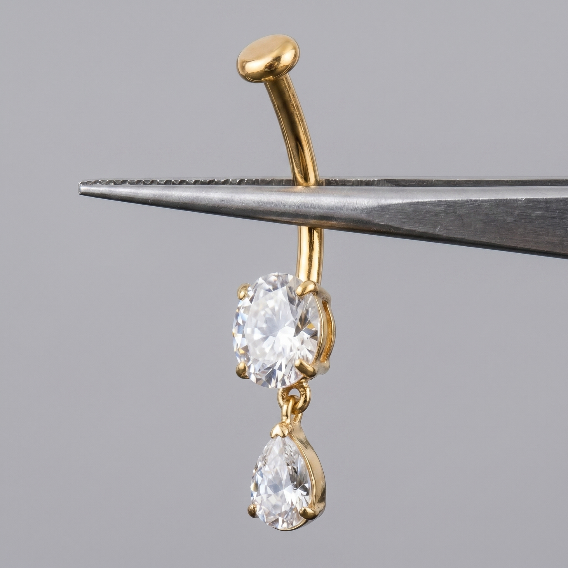 Gold teardrop dangle belly jewelry held by metal tweezers.