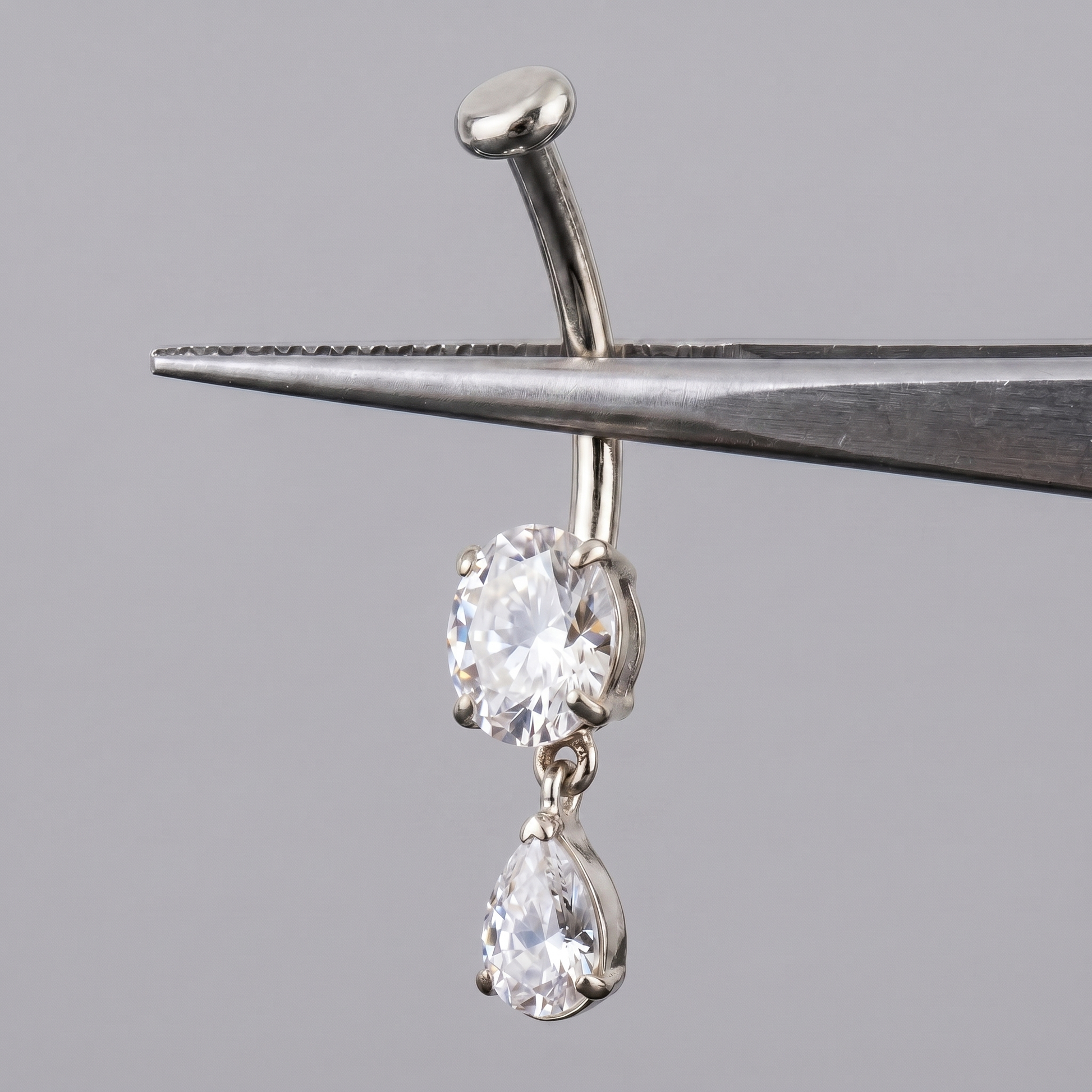 Silver teardrop dangle belly jewelry held by metal tweezers.