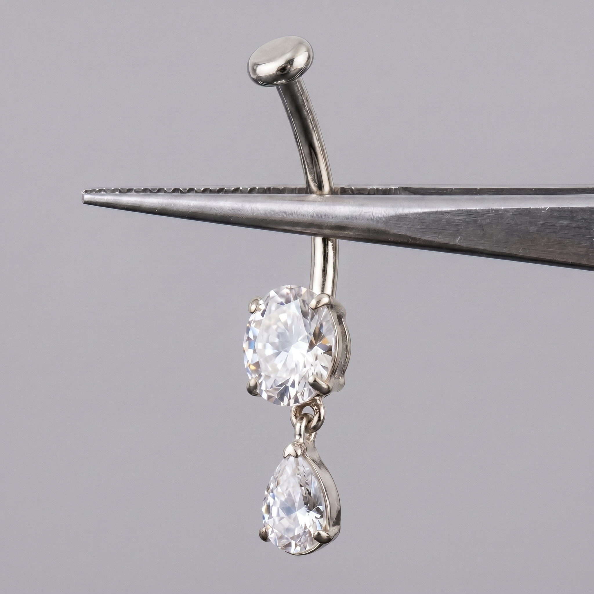 Silver teardrop dangle belly jewelry held by metal tweezers.