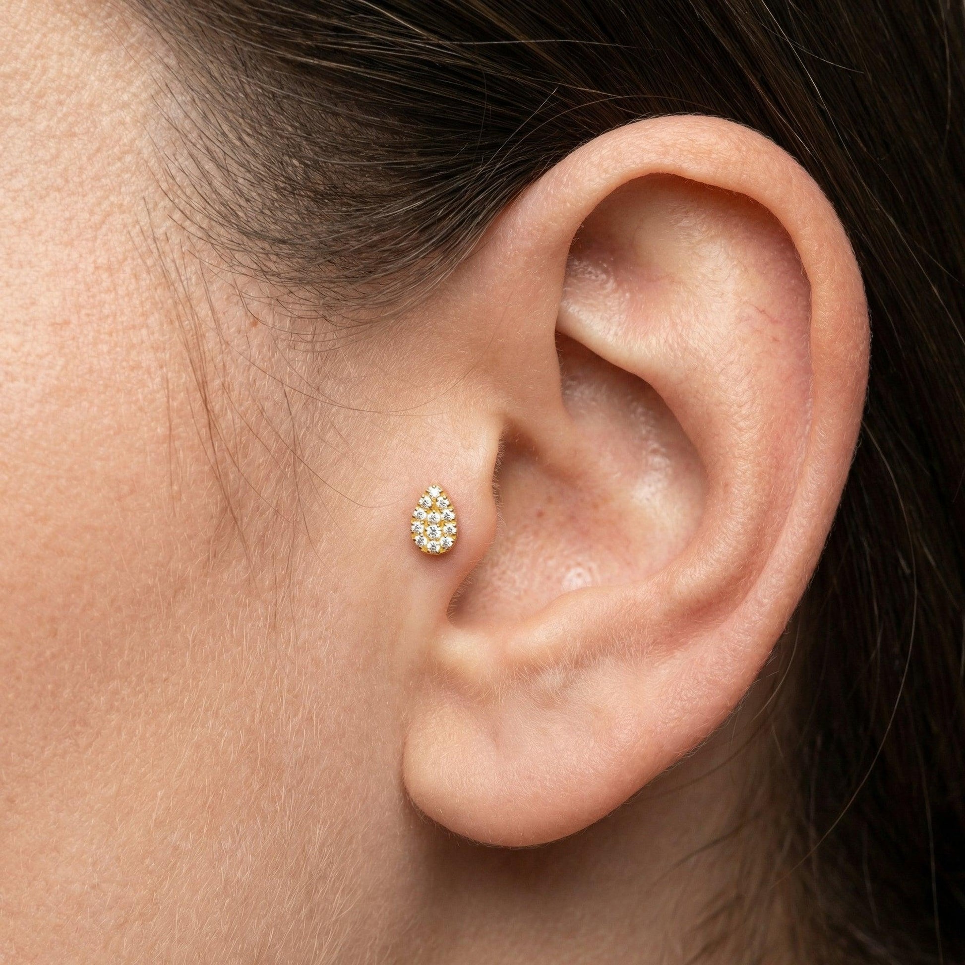 Gold teardrop cartilage stud resting comfortably inside a model's inner piercing placement.