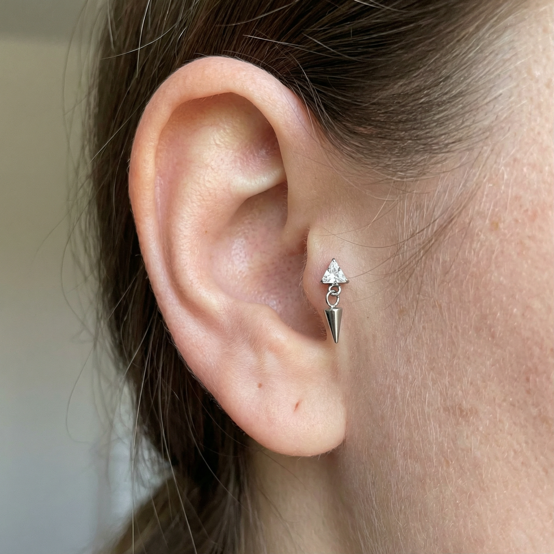 Silver triangle zircon spike dangle stud styled beautifully inside a model's piercing.