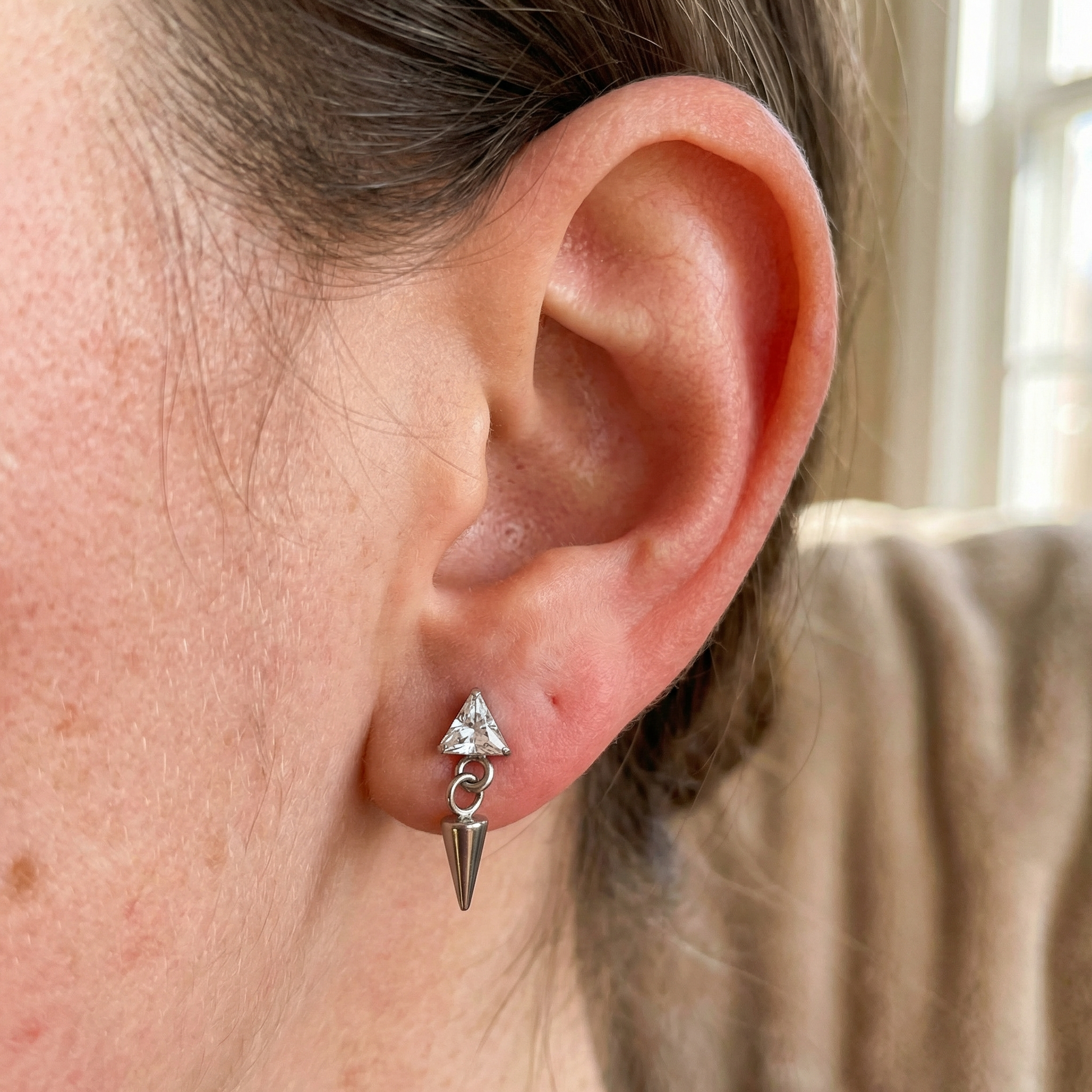 Silver triangle zircon dangling spike cartilage earring styled cleanly in a standard