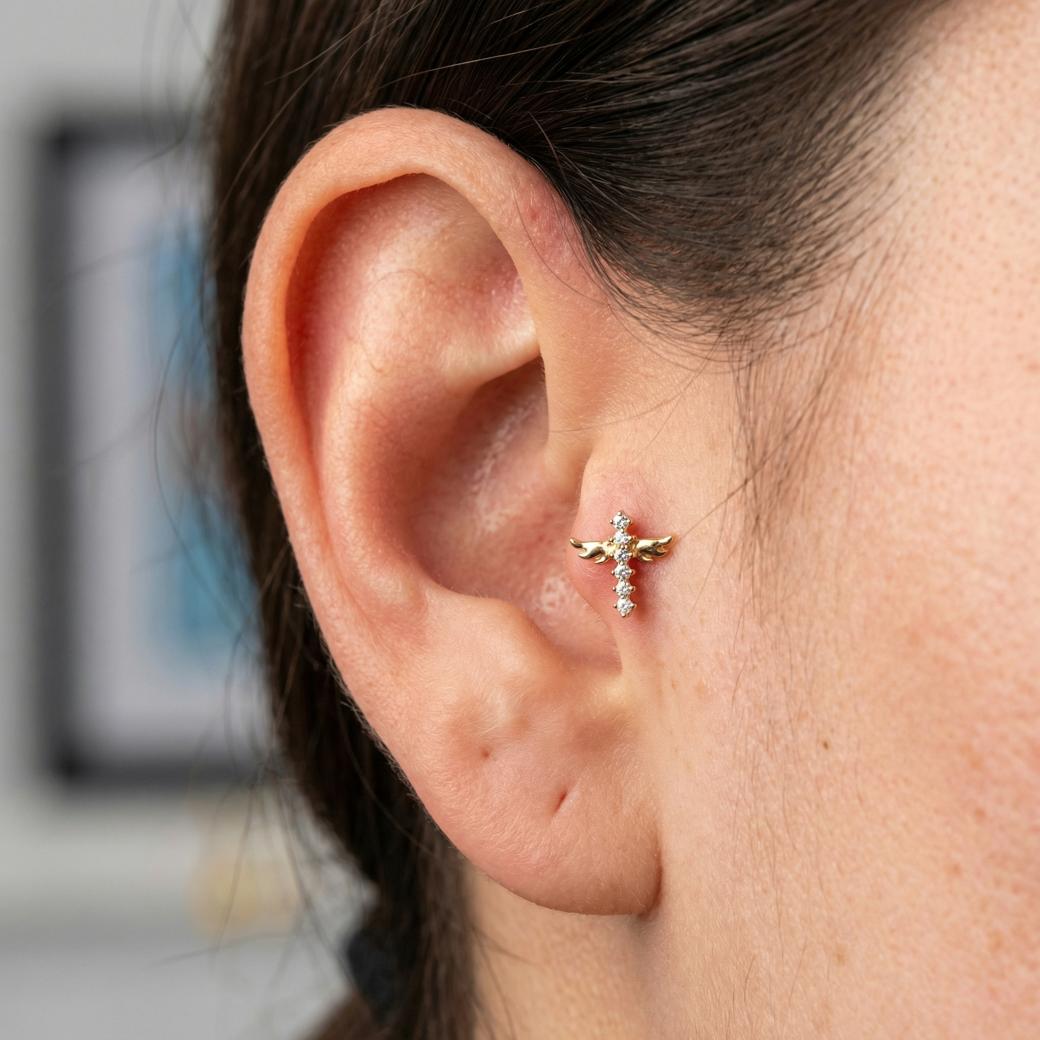 Model showcasing a gold winged cross zircon in a piercing.