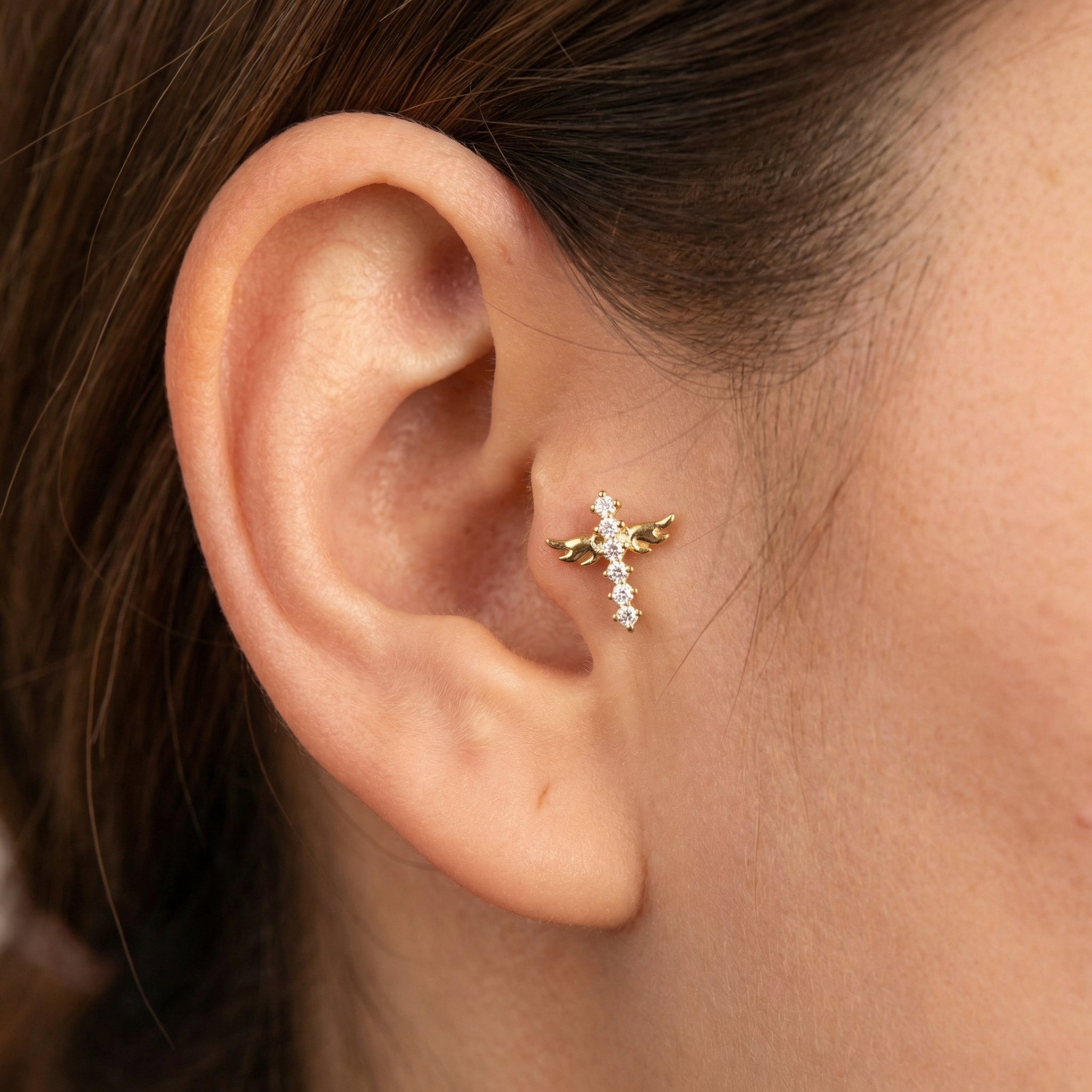 Gold winged cross zircon styled beautifully on a model's inner ear piercing.