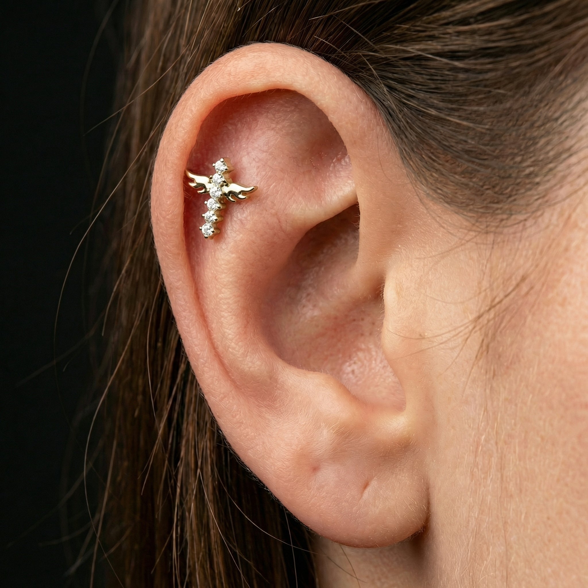 Close-up of a silver winged cross worn in a model's outer cartilage