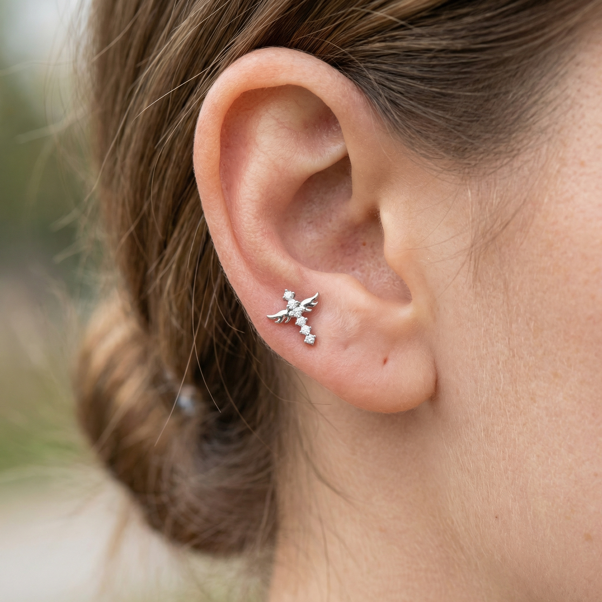 Model profile displaying a silver winged cross in her piercing.