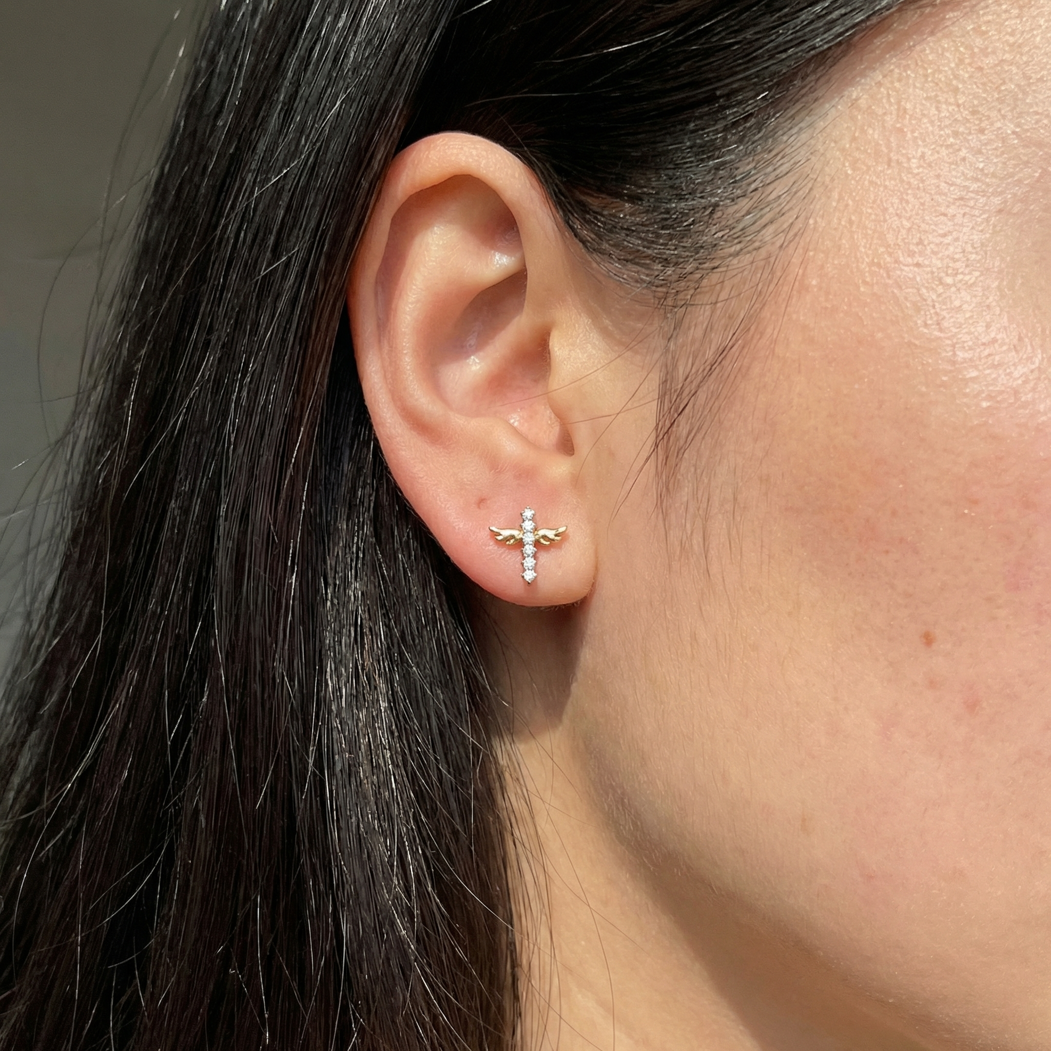 Model showcasing a gold winged cross in her standard lower piercing.