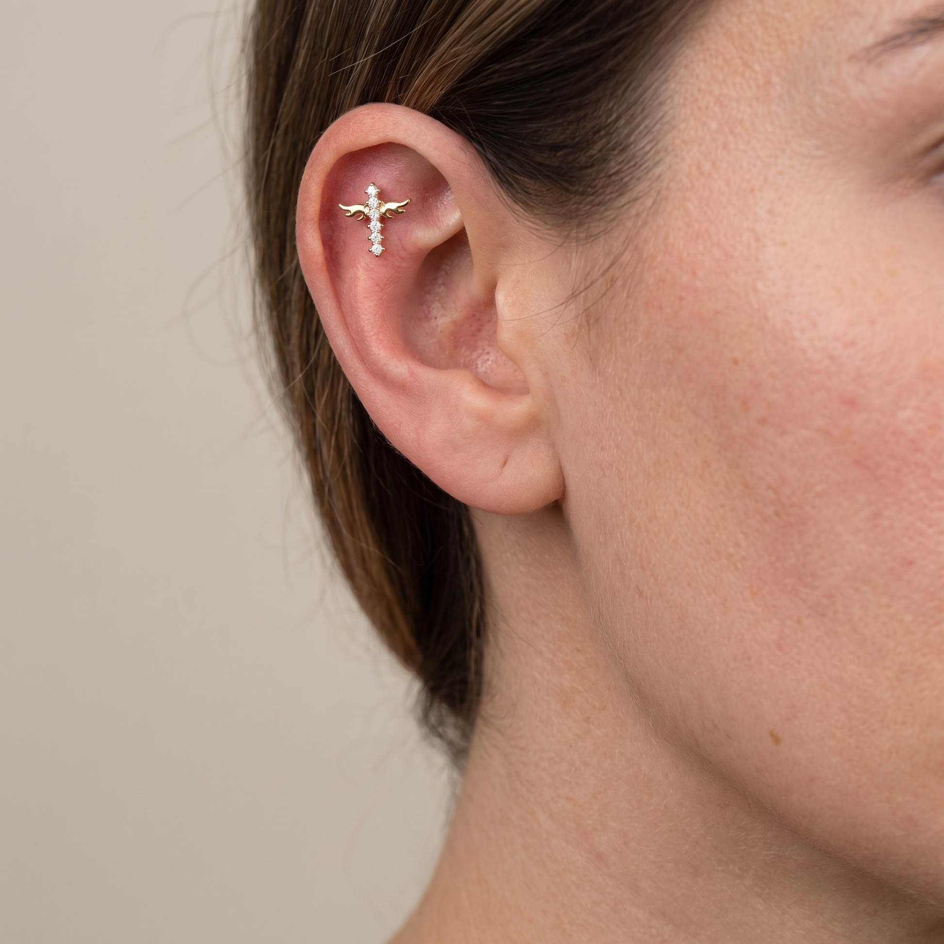 Gold winged cross zircon styled perfectly on a model's ear cartilage piercing.