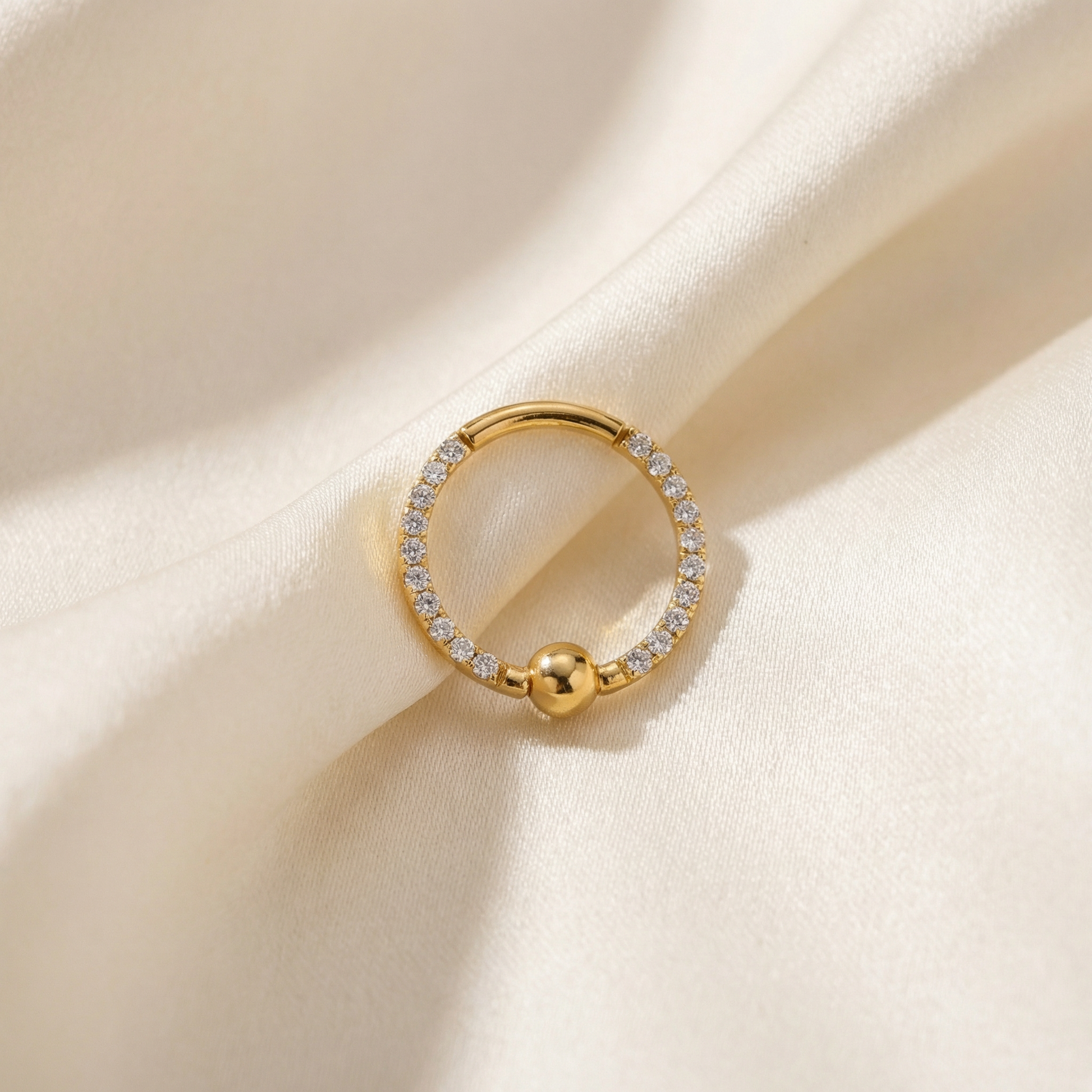 Gold zircon center bead clicker hoop resting elegantly on soft cream silk